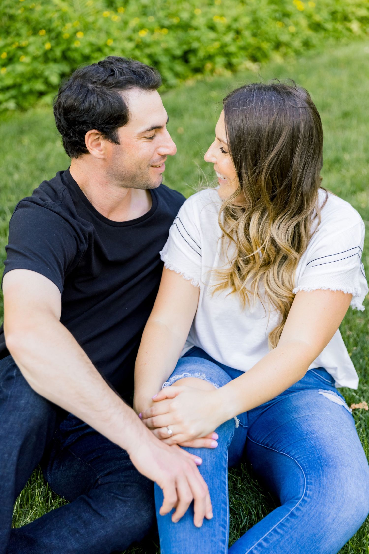 A couple sits together on grass sharing an intimate moment in a sunny outdoor setting.