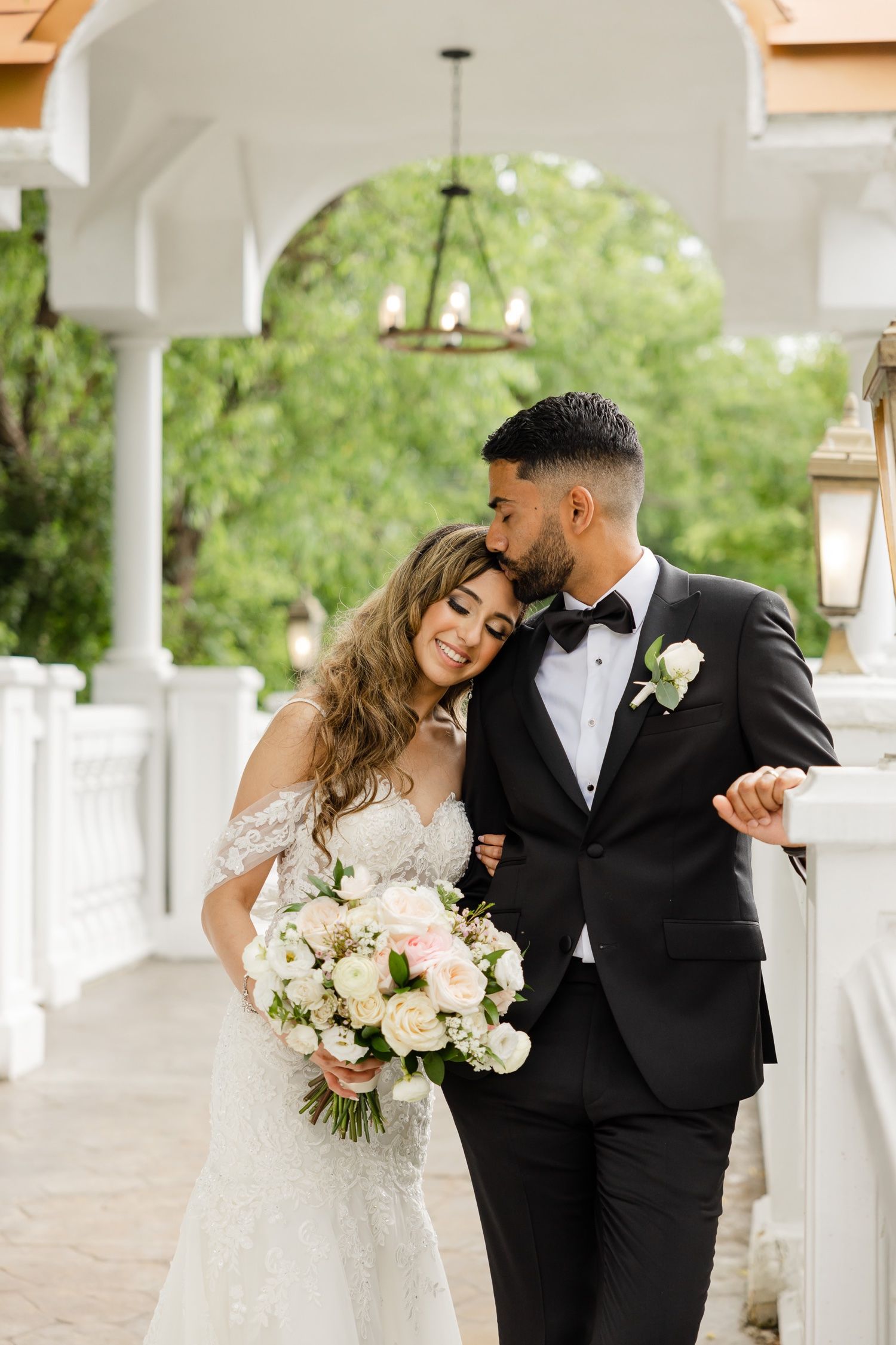 Romantic wedding moment captured on an elegant white columned terrace with hanging lanterns.