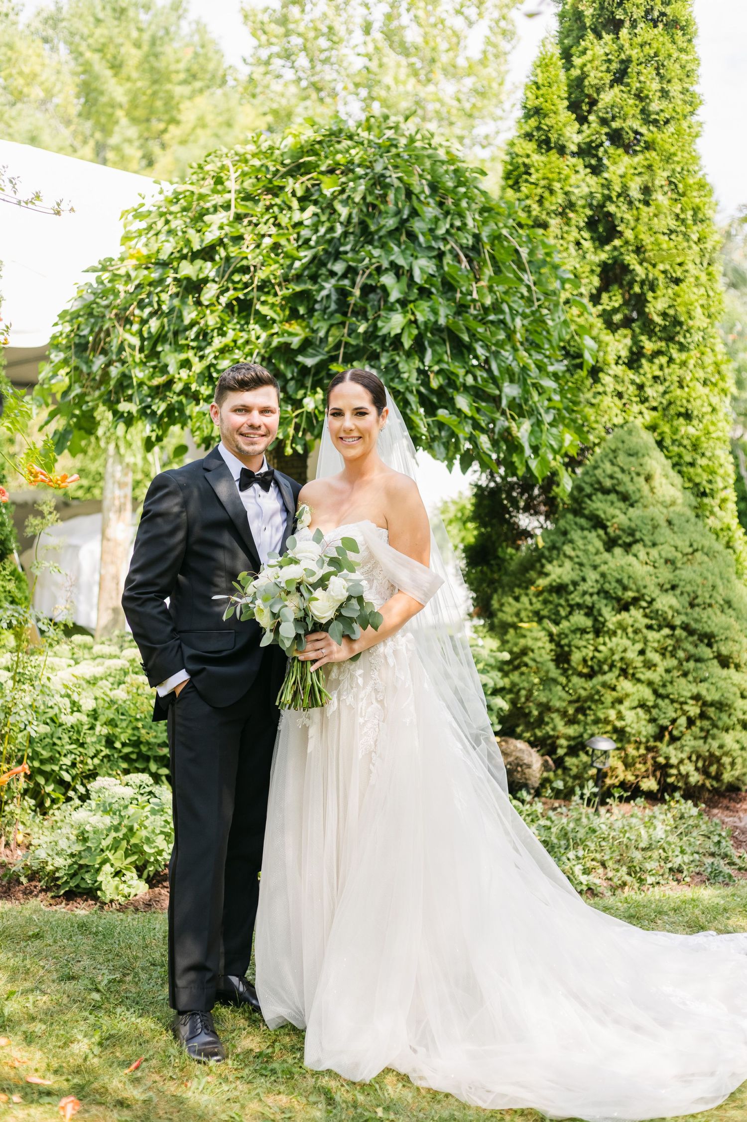Classic wedding portrait of couple standing in front of lush greenery and garden backdrop.