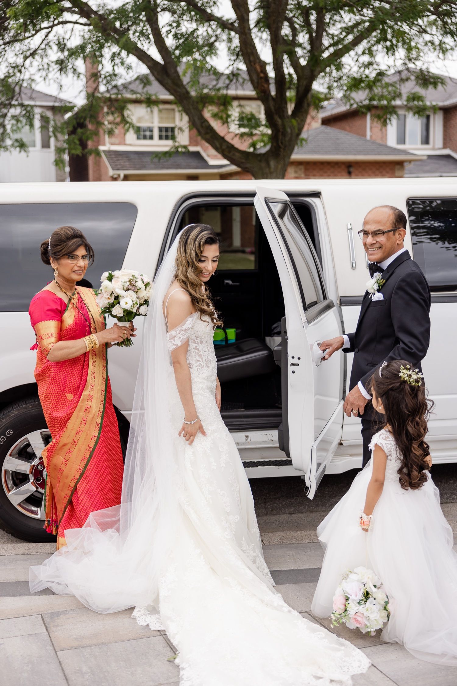 Wedding party assists bride entering white limousine while flower girl holds bouquet.