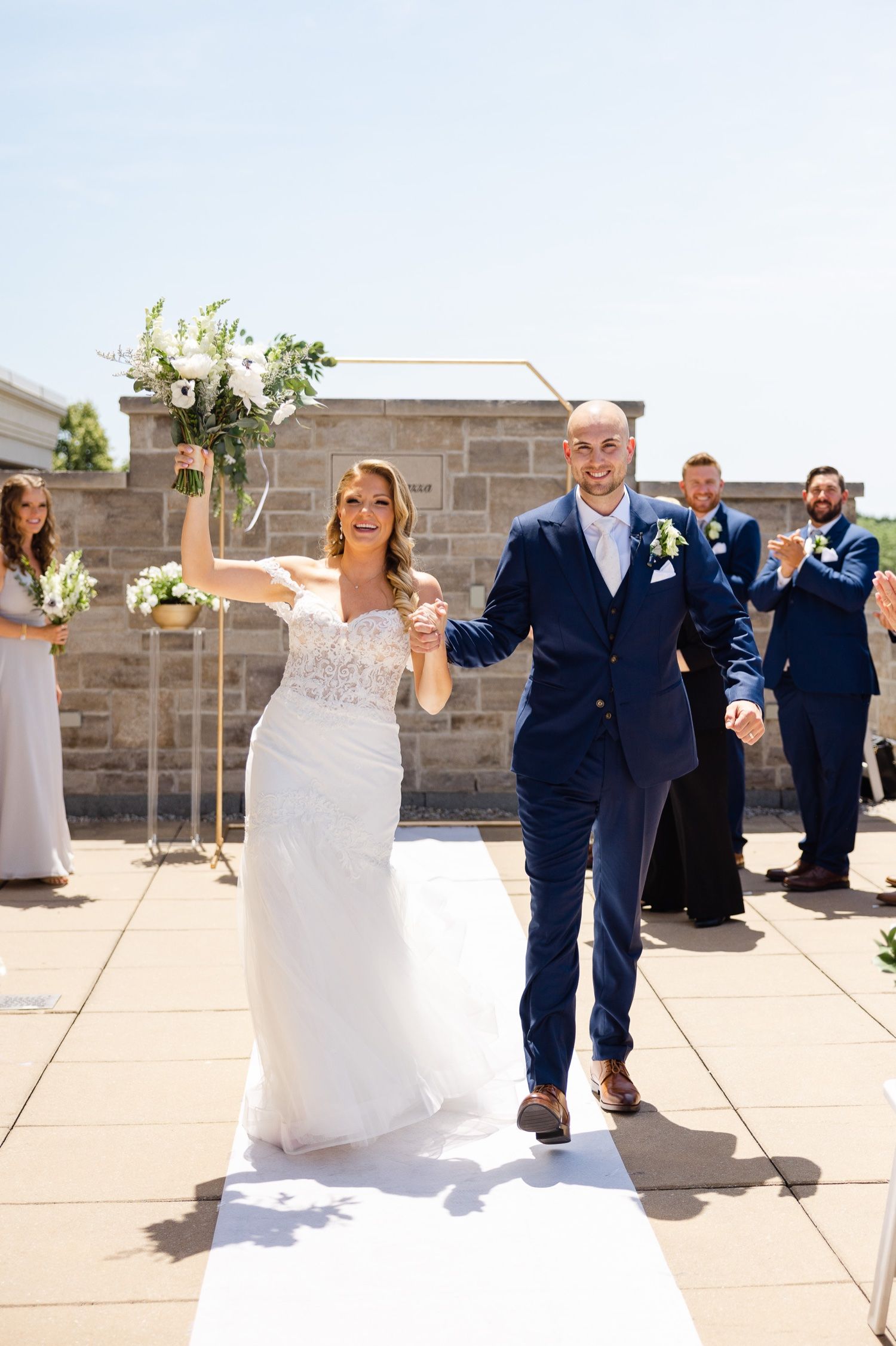 Newlyweds celebrate joyfully as they exit their rooftop wedding ceremony holding beautiful white bouquet.