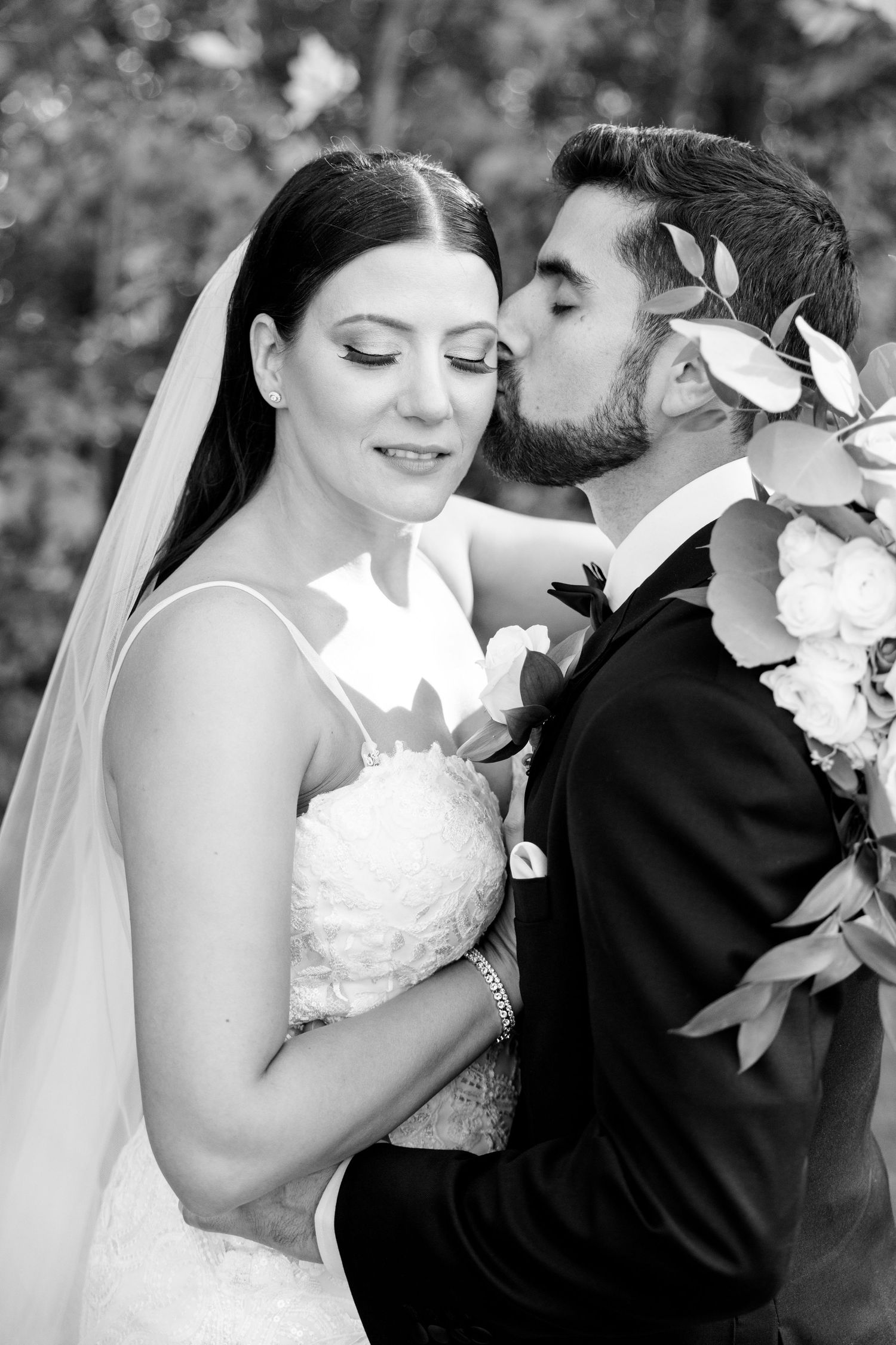 Black and white close-up portrait captures tender wedding moment with white flowers.