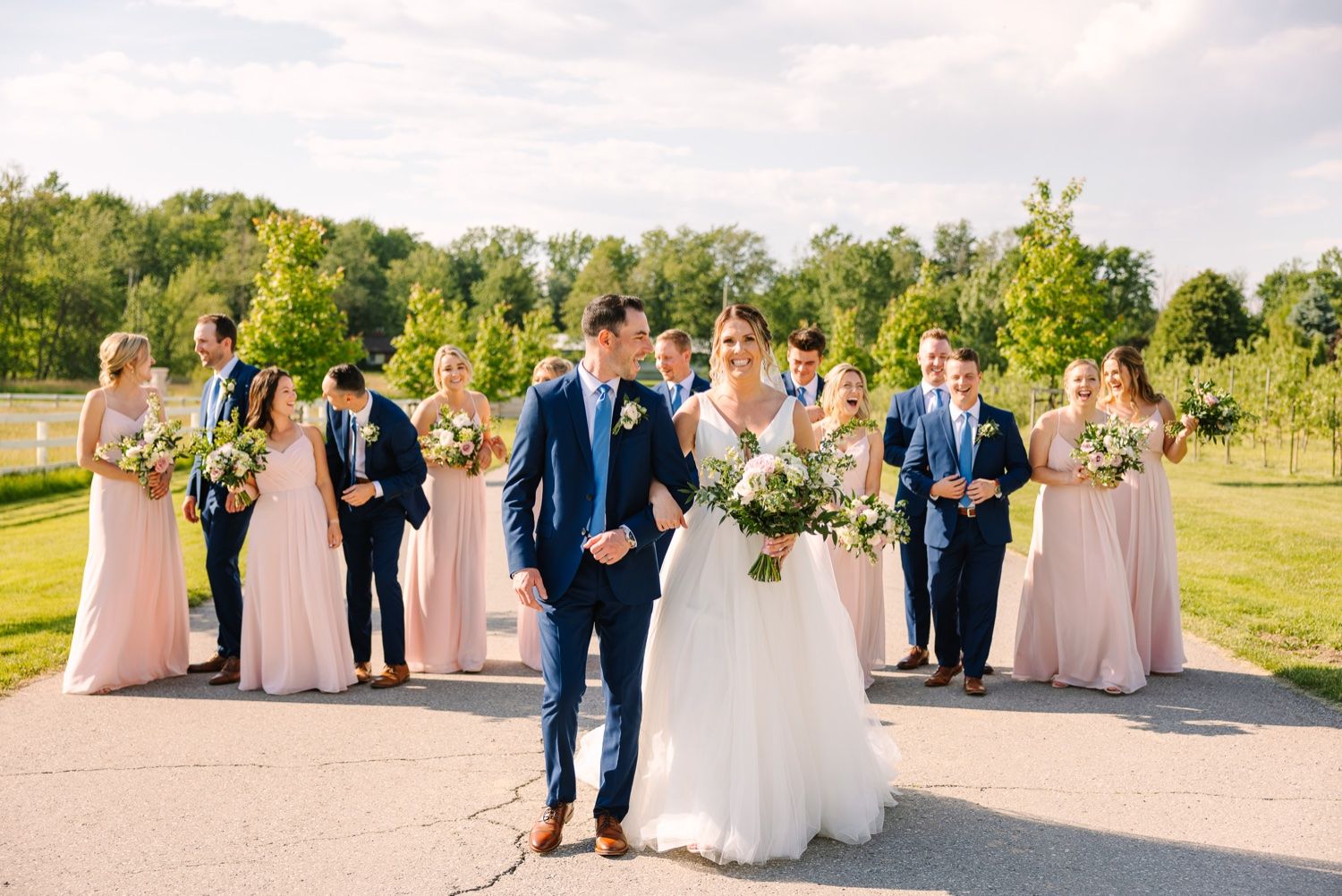 Wedding party poses on outdoor pathway with bridesmaids in pink and groomsmen in navy blue.