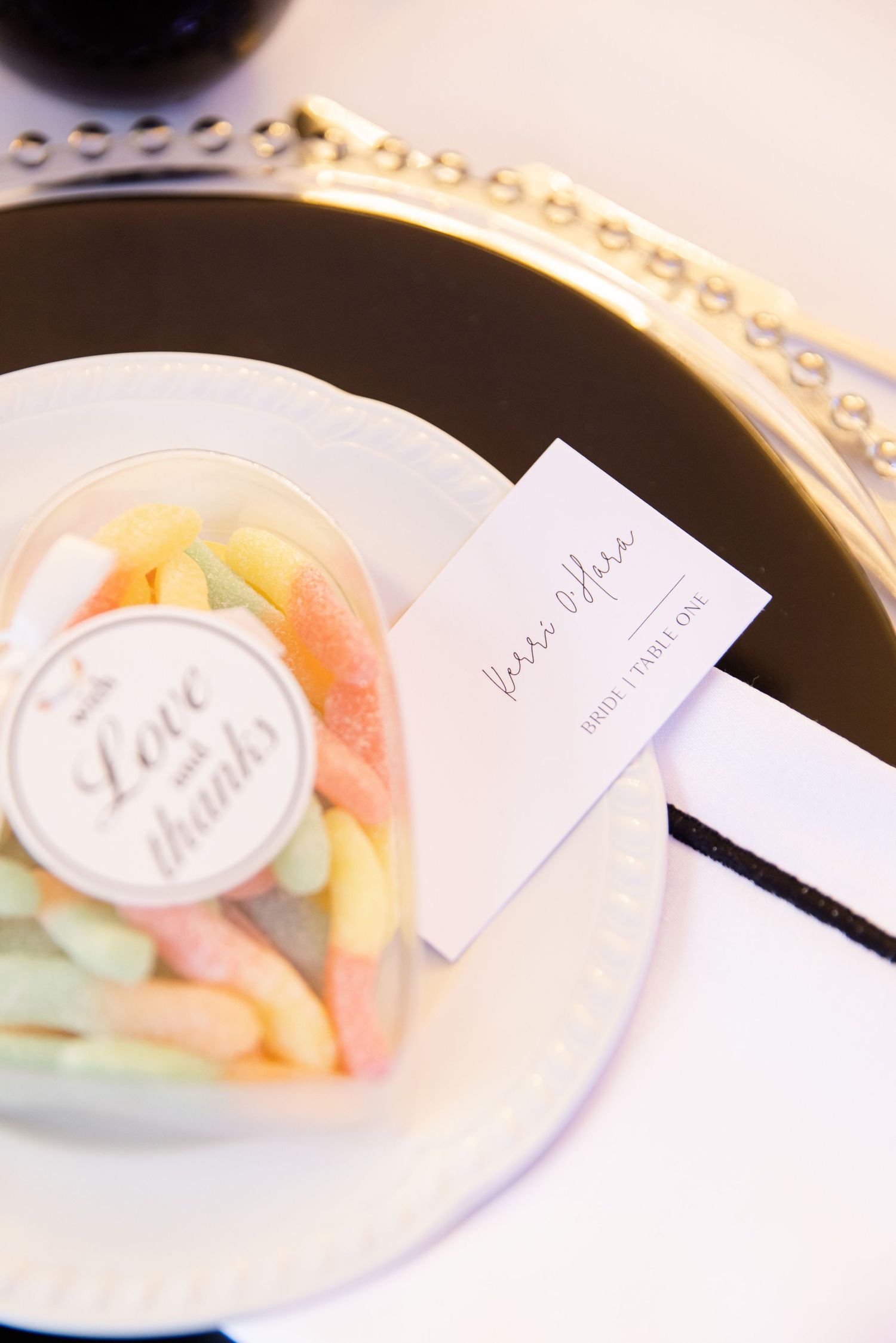Close-up of wedding favor candy in clear container on ornate gold-rimmed plate with place card.