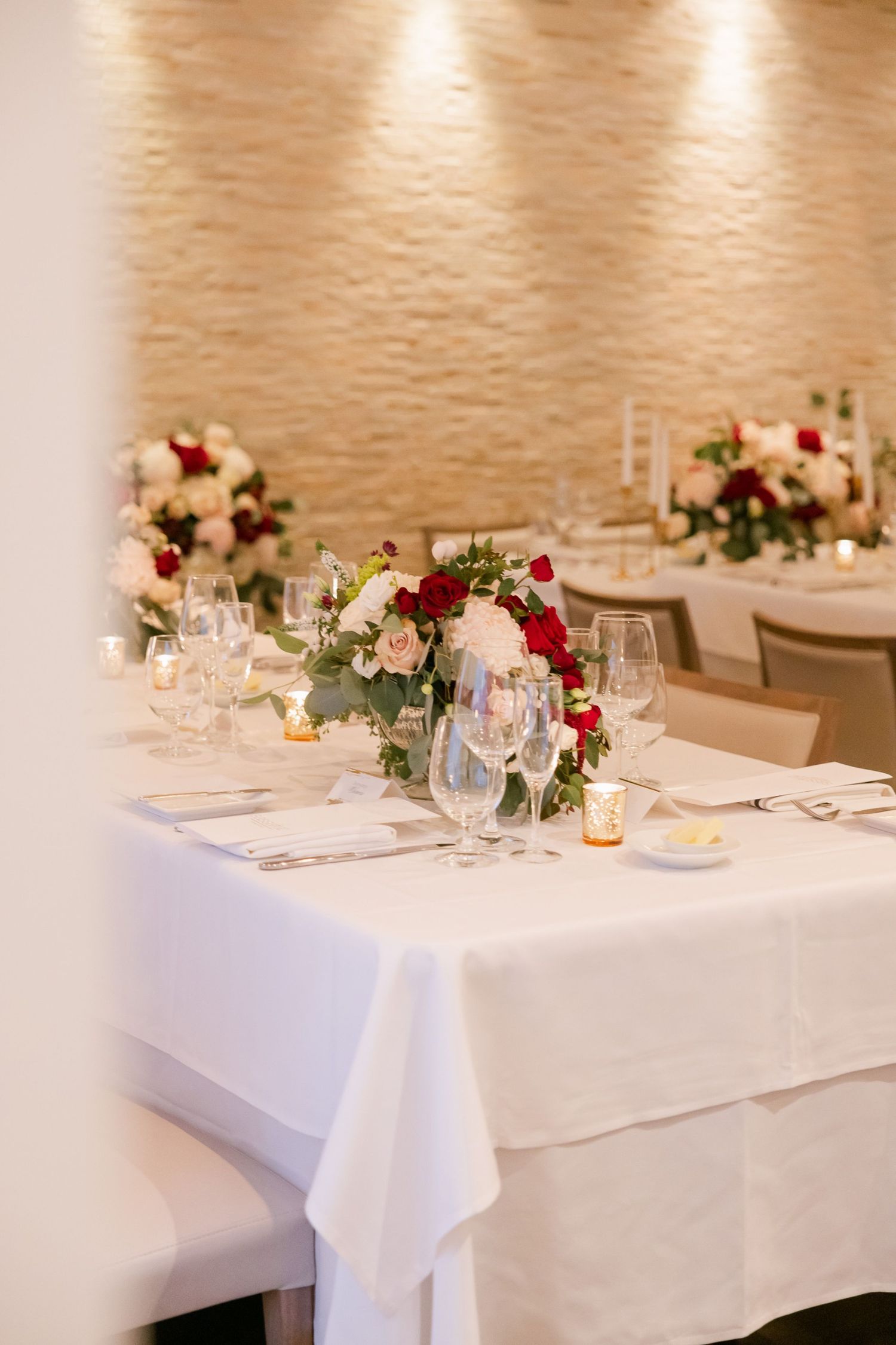 An elegant wedding reception table with red and white floral centerpieces and crystal glassware.