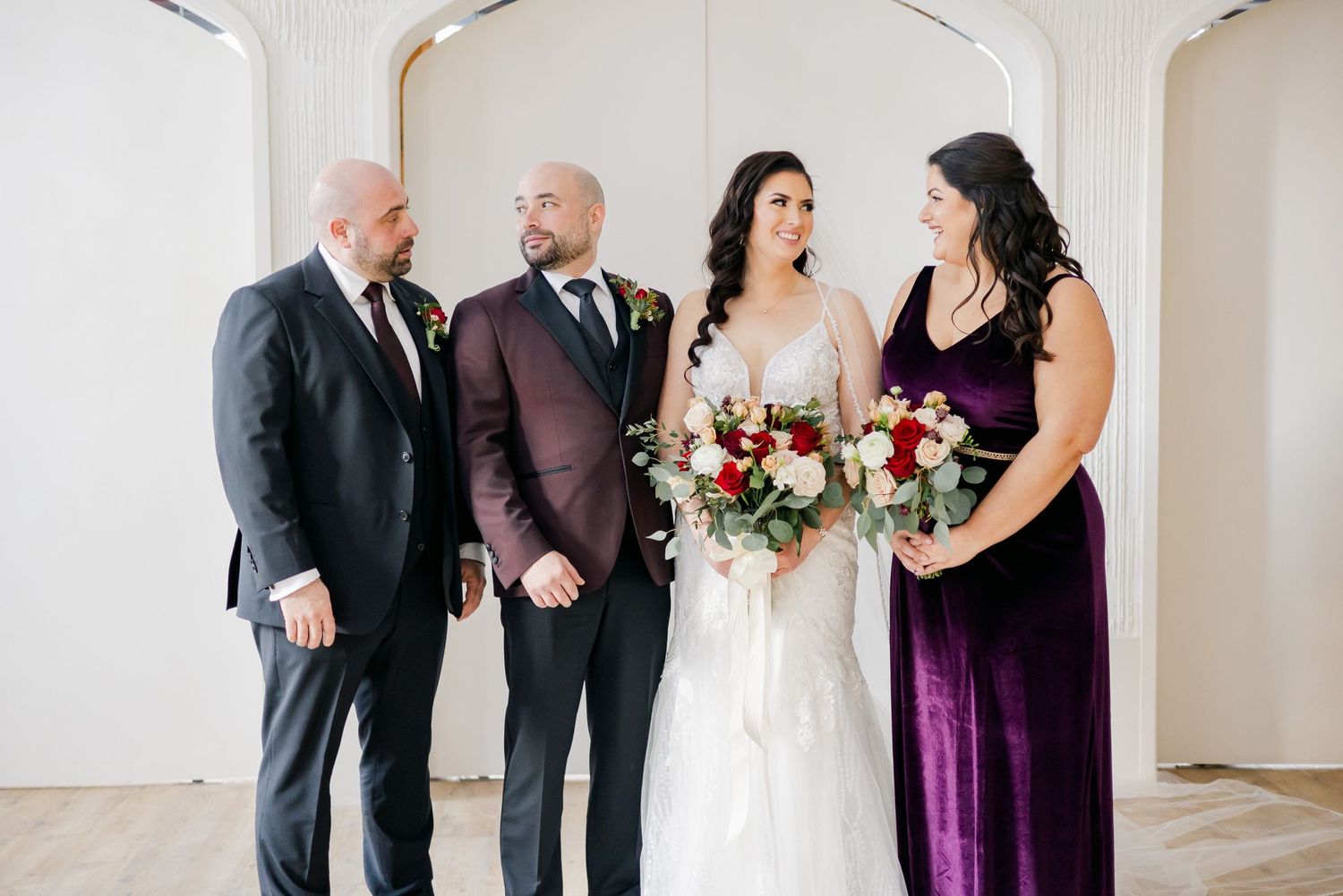 Wedding group shares candid moment under elegant white archway.