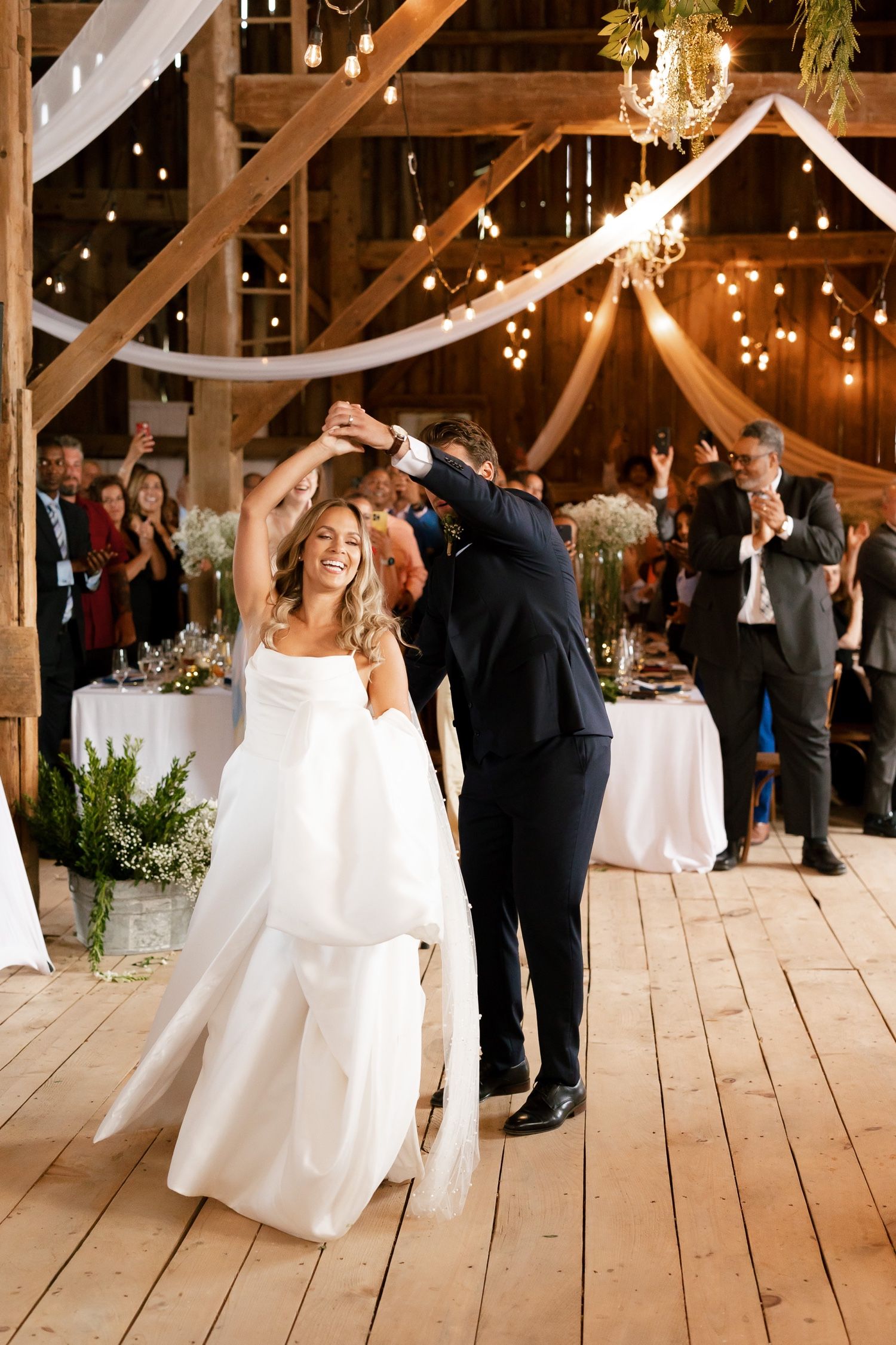 Celebratory dance moment in rustic barn venue with white draping and string lights.