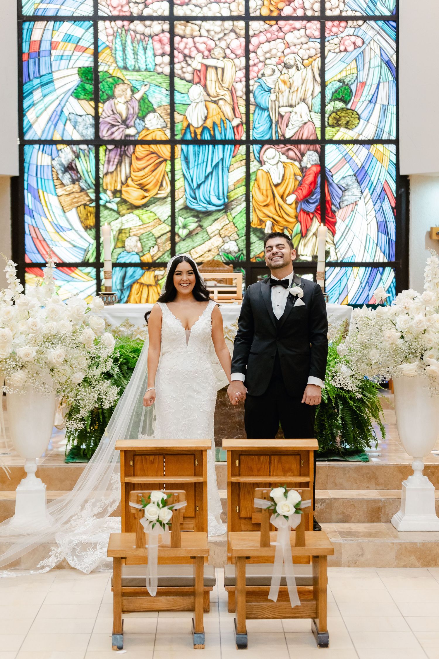 Wedding portrait with couple standing before colorful stained glass and floral decorations.