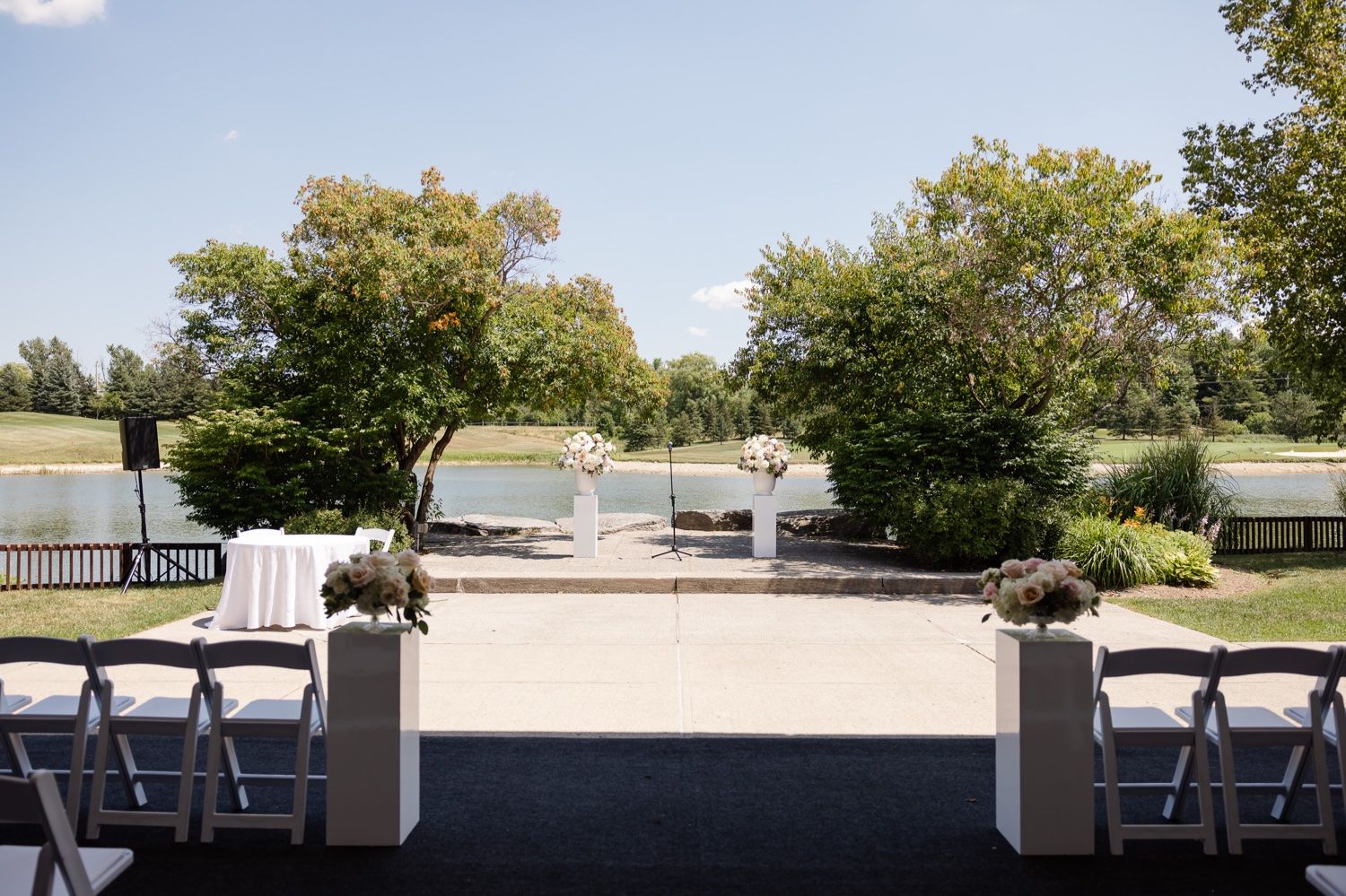 Outdoor wedding ceremony space overlooking a lake with white chairs and decorative pillars.