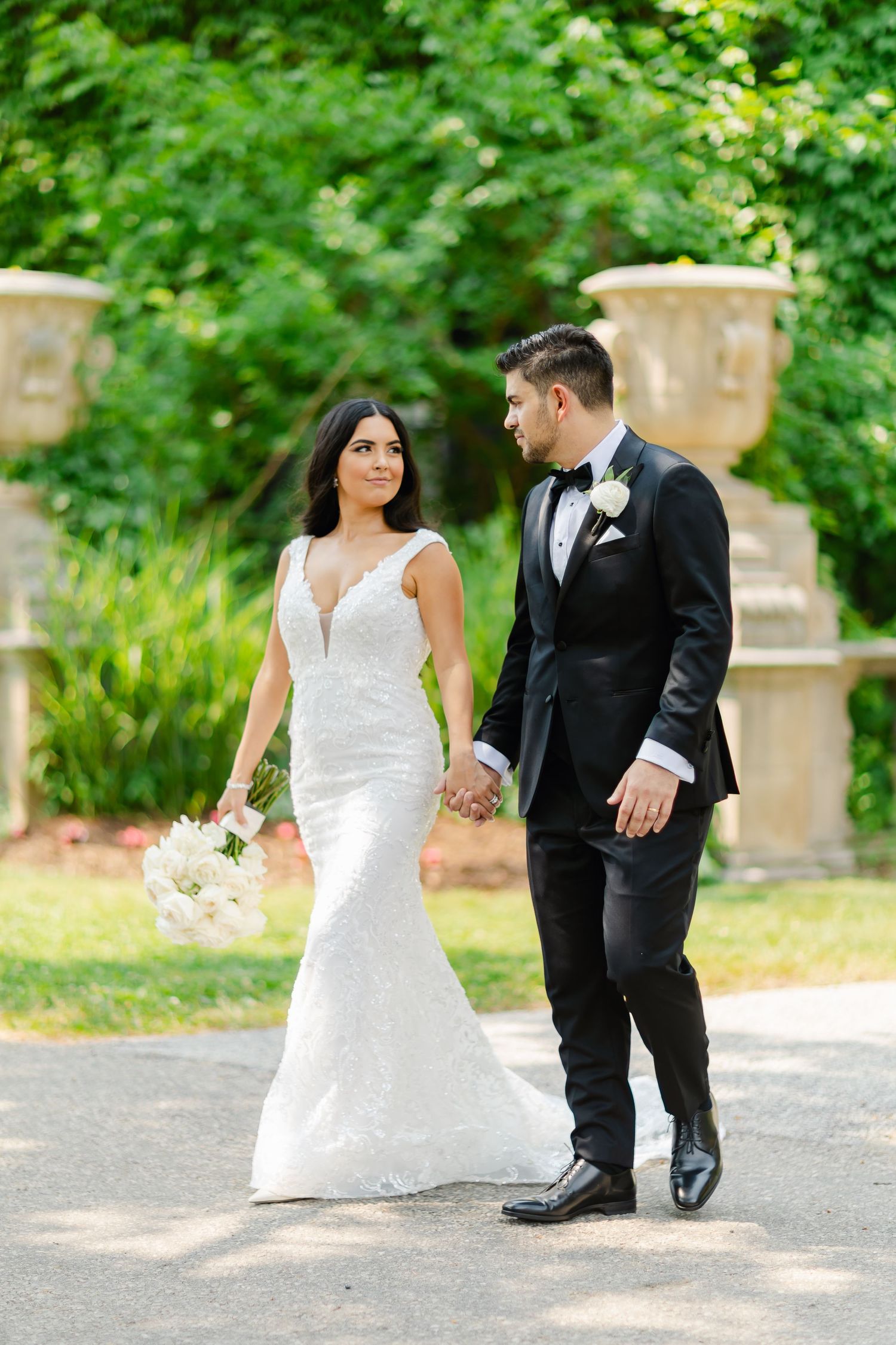 A couple takes a romantic wedding day stroll through a garden setting with stone urns.