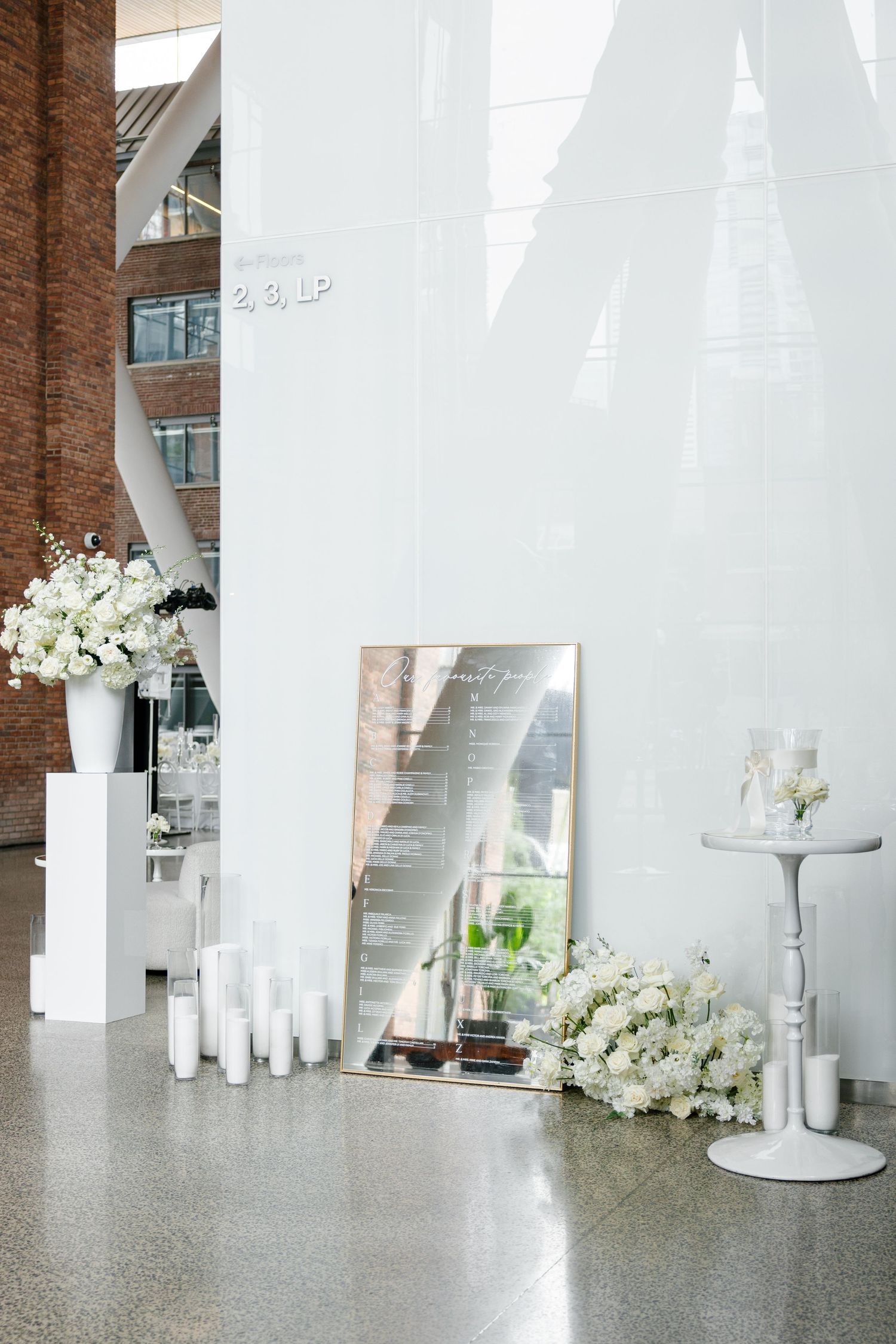 Modern event space decor featuring mirror signage, white flowers and candles against minimalist white walls.