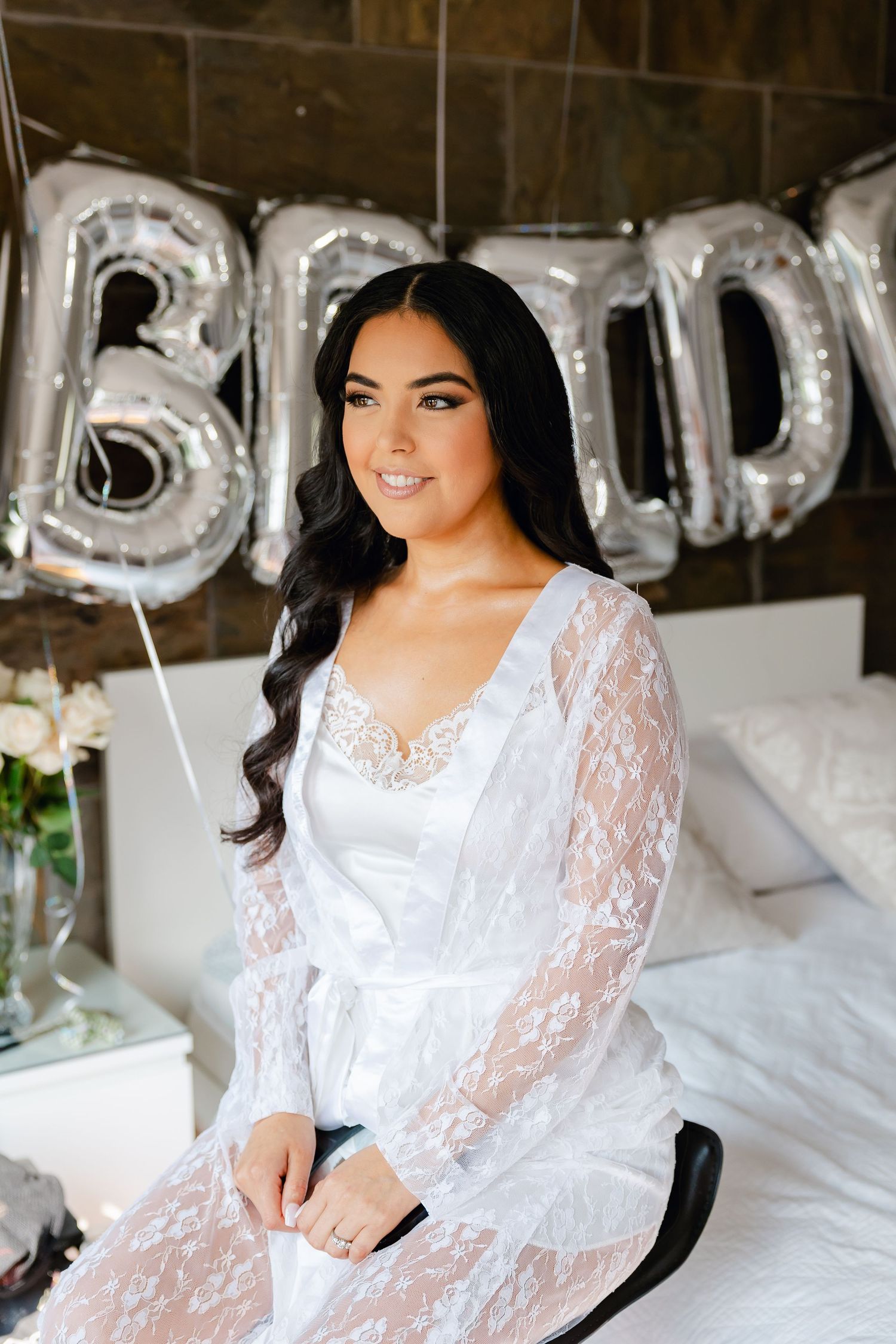 A formal bridal boudoir setting with silver balloon letters and white lace robe.