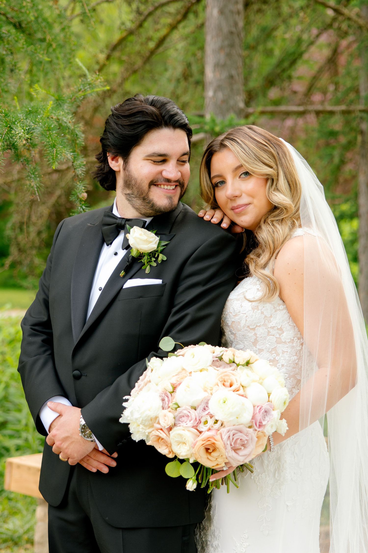 Close up portrait of couple with pink bouquet against verdant garden background.