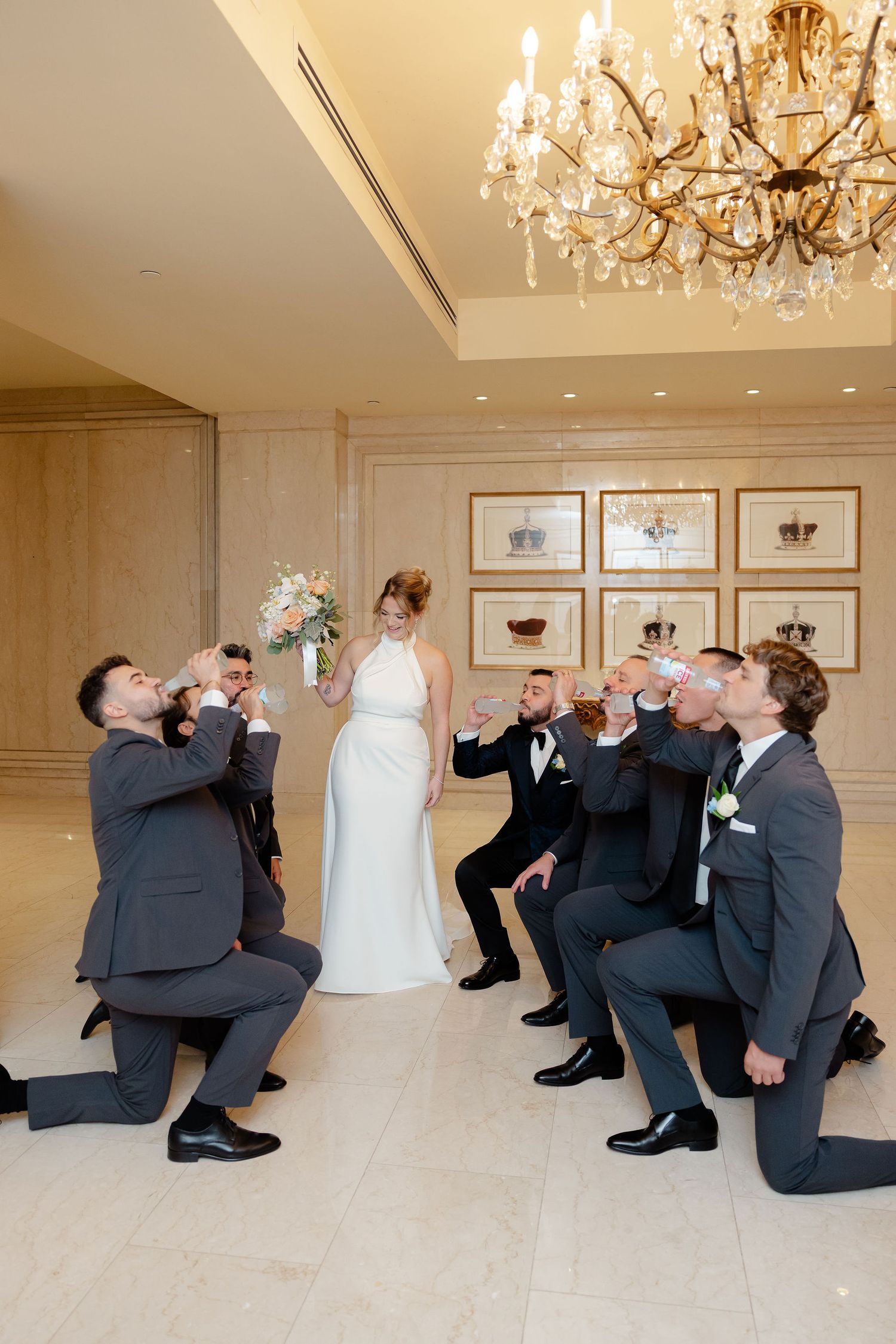Wedding party performs synchronized bowing poses in a luxurious ballroom setting.