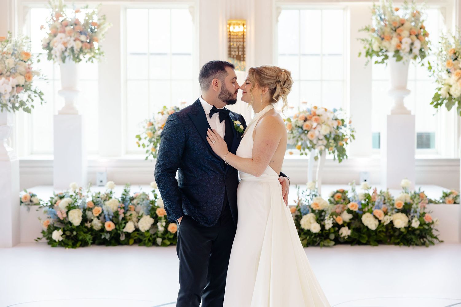 Romantic wedding ceremony setup with floral arch and white decor in a bright sunlit room.