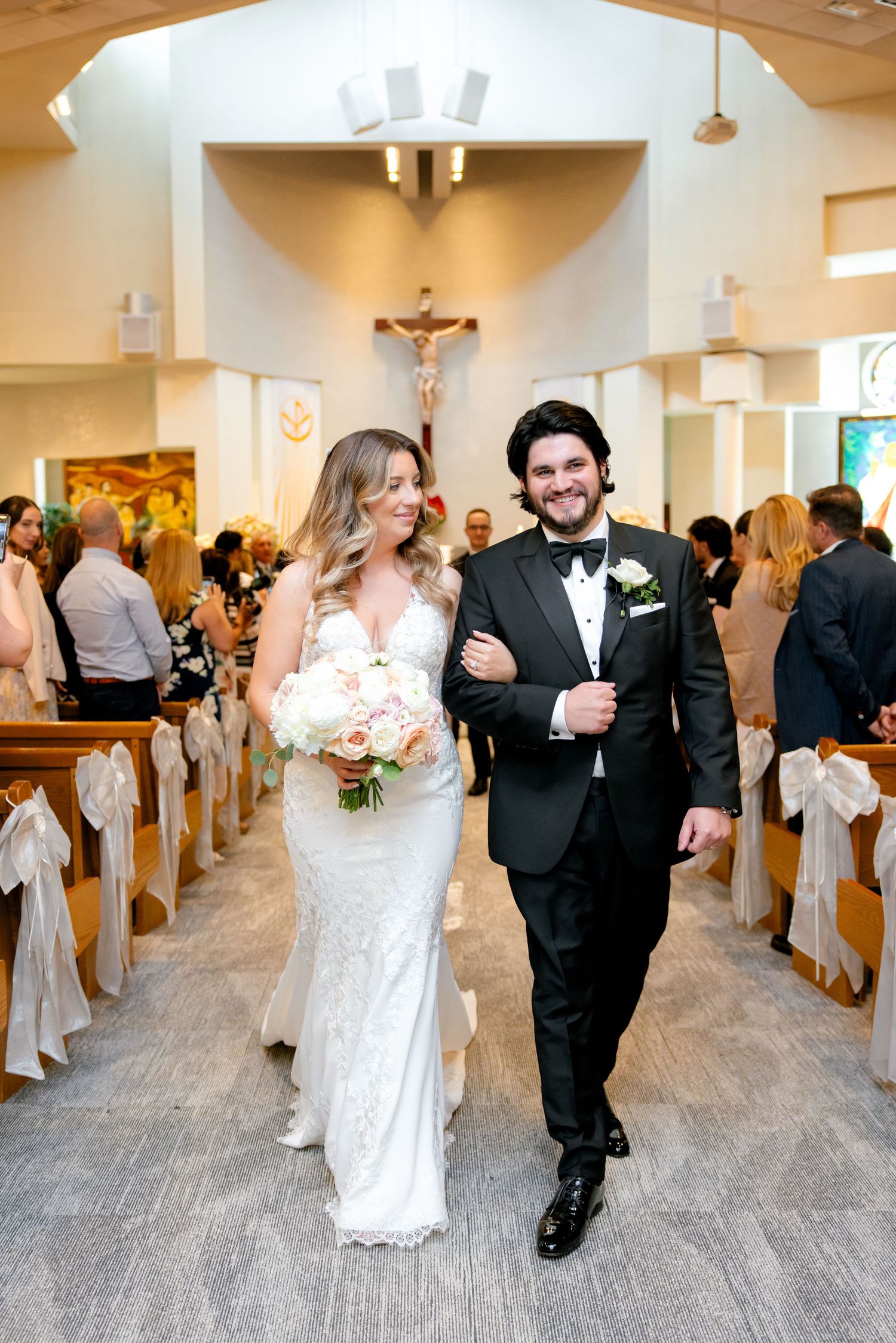 Happy wedding couple walking arm in arm down the decorated church aisle.