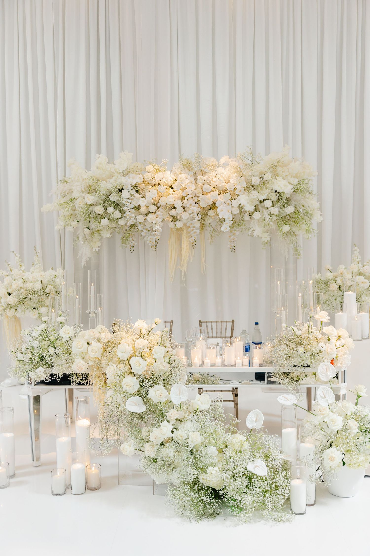 Ethereal white wedding reception setup with suspended floral arrangements and candle lighting.