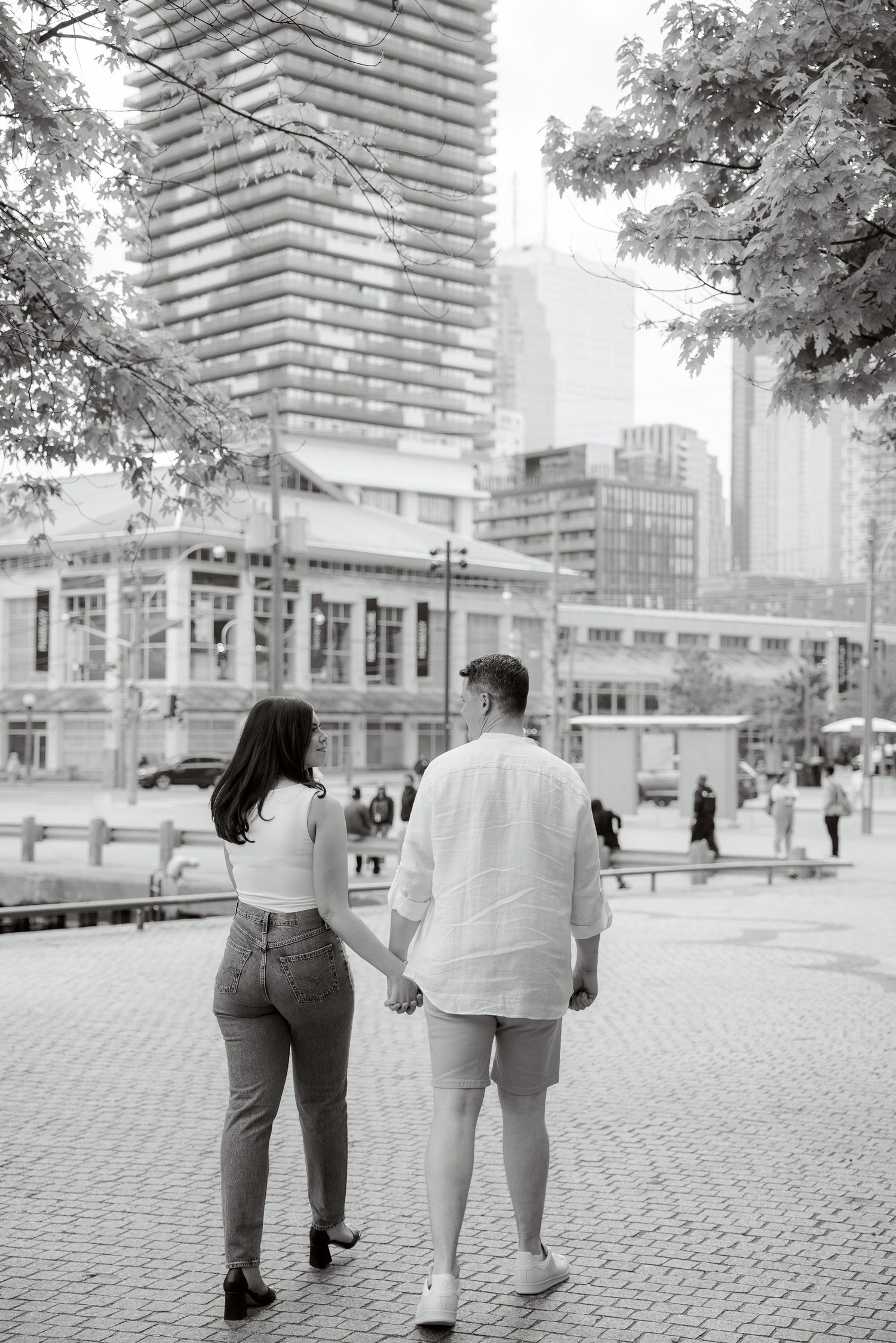 Couple walking hand in hand through urban setting with skyscrapers in background.