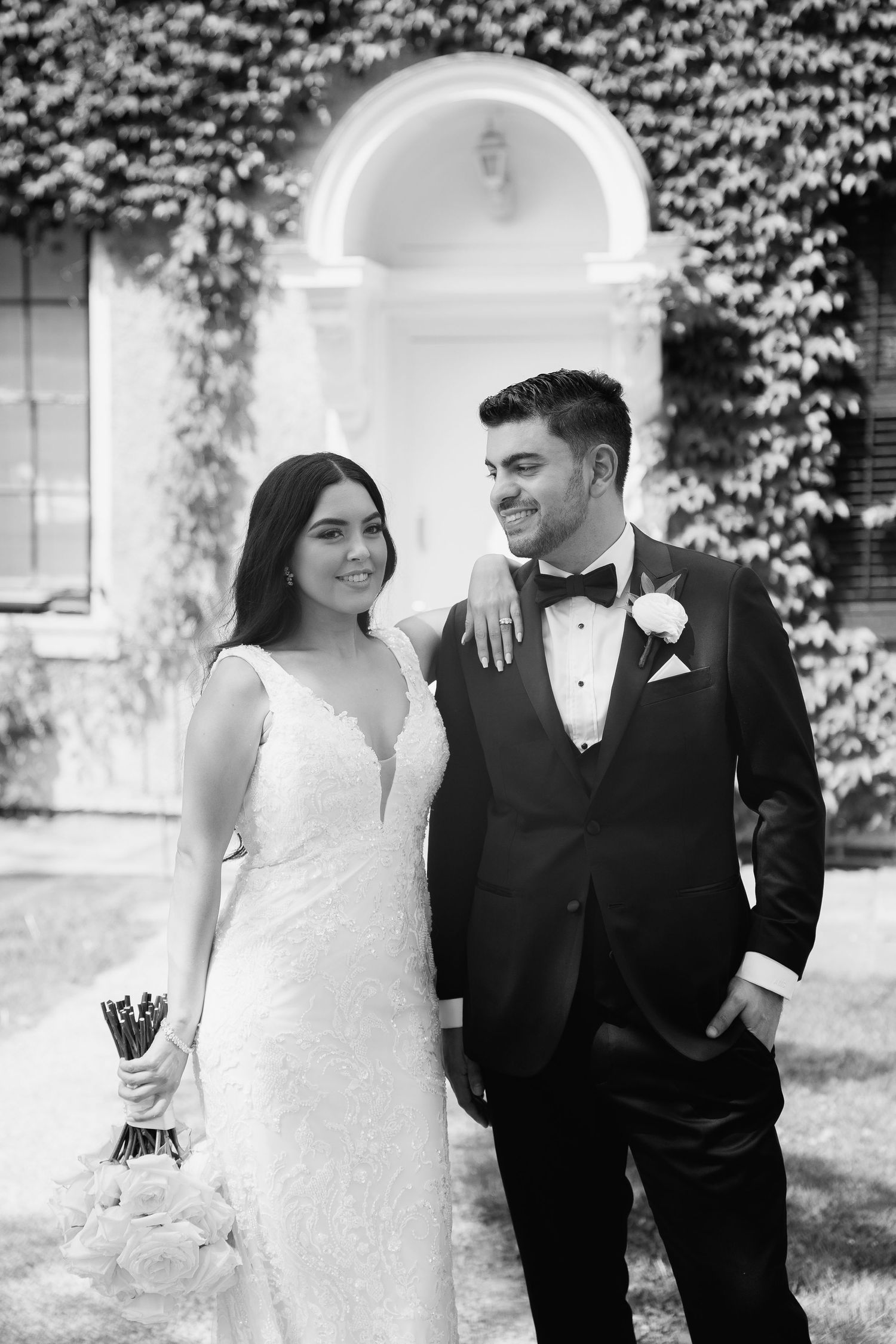 A joyful wedding couple poses together in front of an ivy-covered archway.