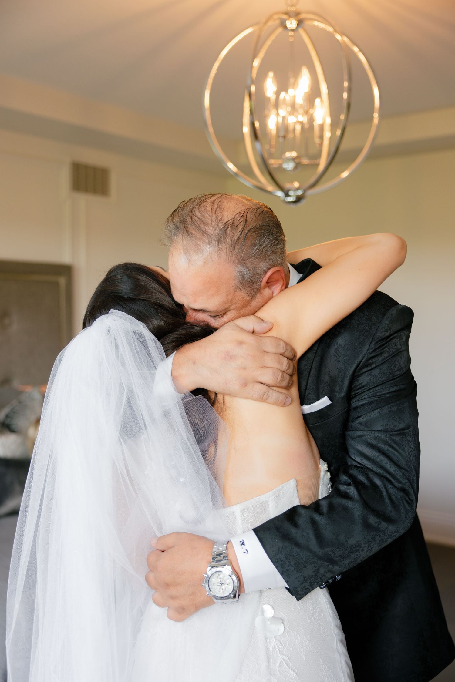 Emotional embrace under an elegant spherical chandelier.