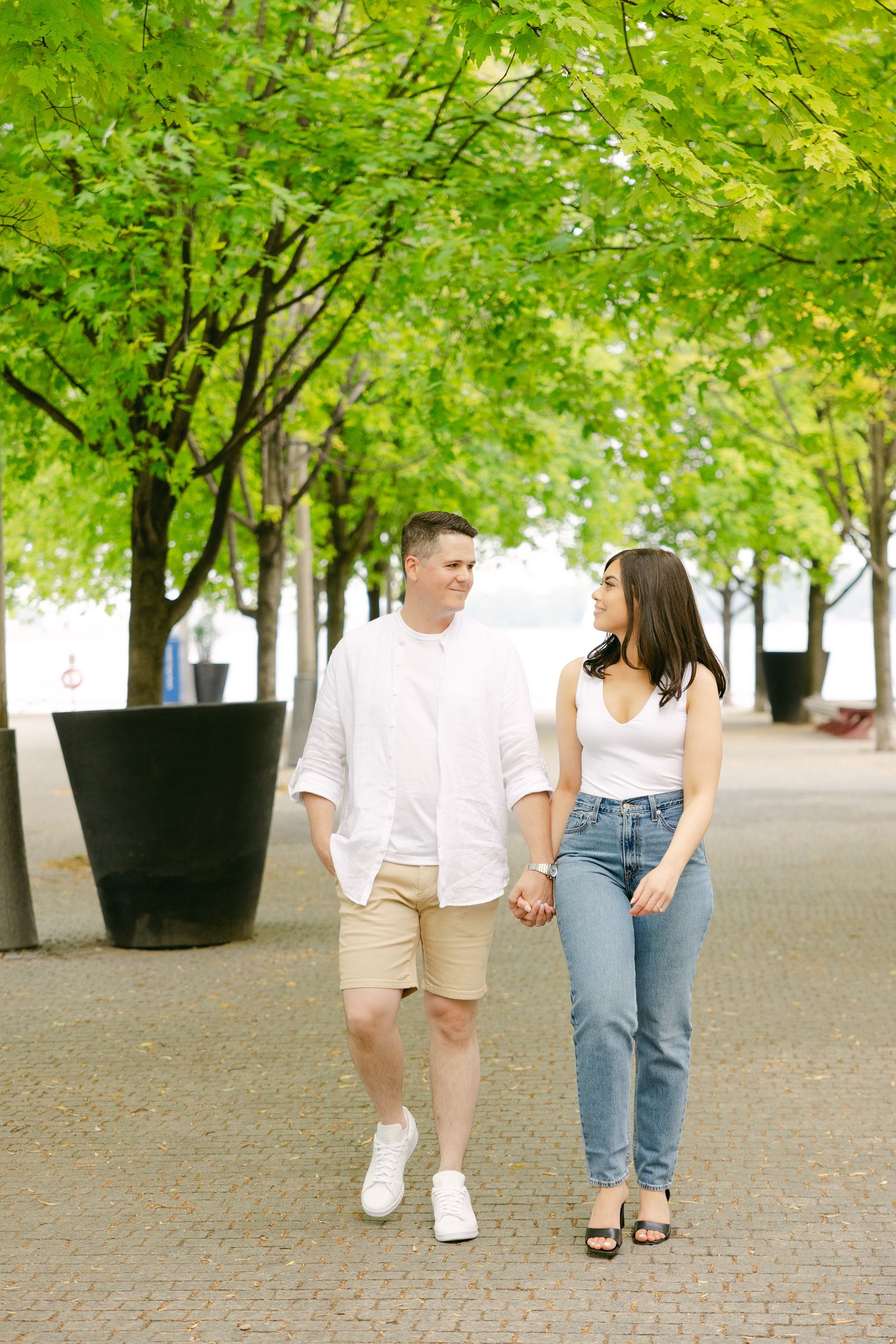 A couple takes a romantic walk under a lush green canopy of trees.