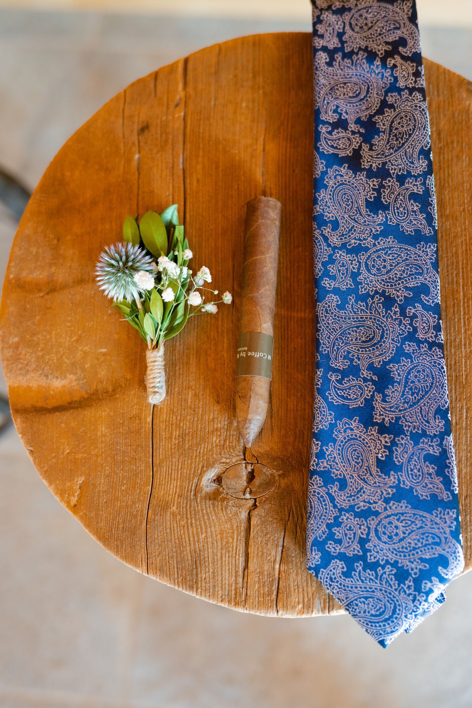 Blue paisley tie and delicate white floral boutonniere displayed on wooden table surface.