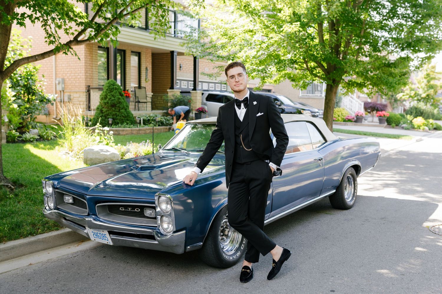 Classic blue GTO muscle car parked on a residential street with person in formal attire.