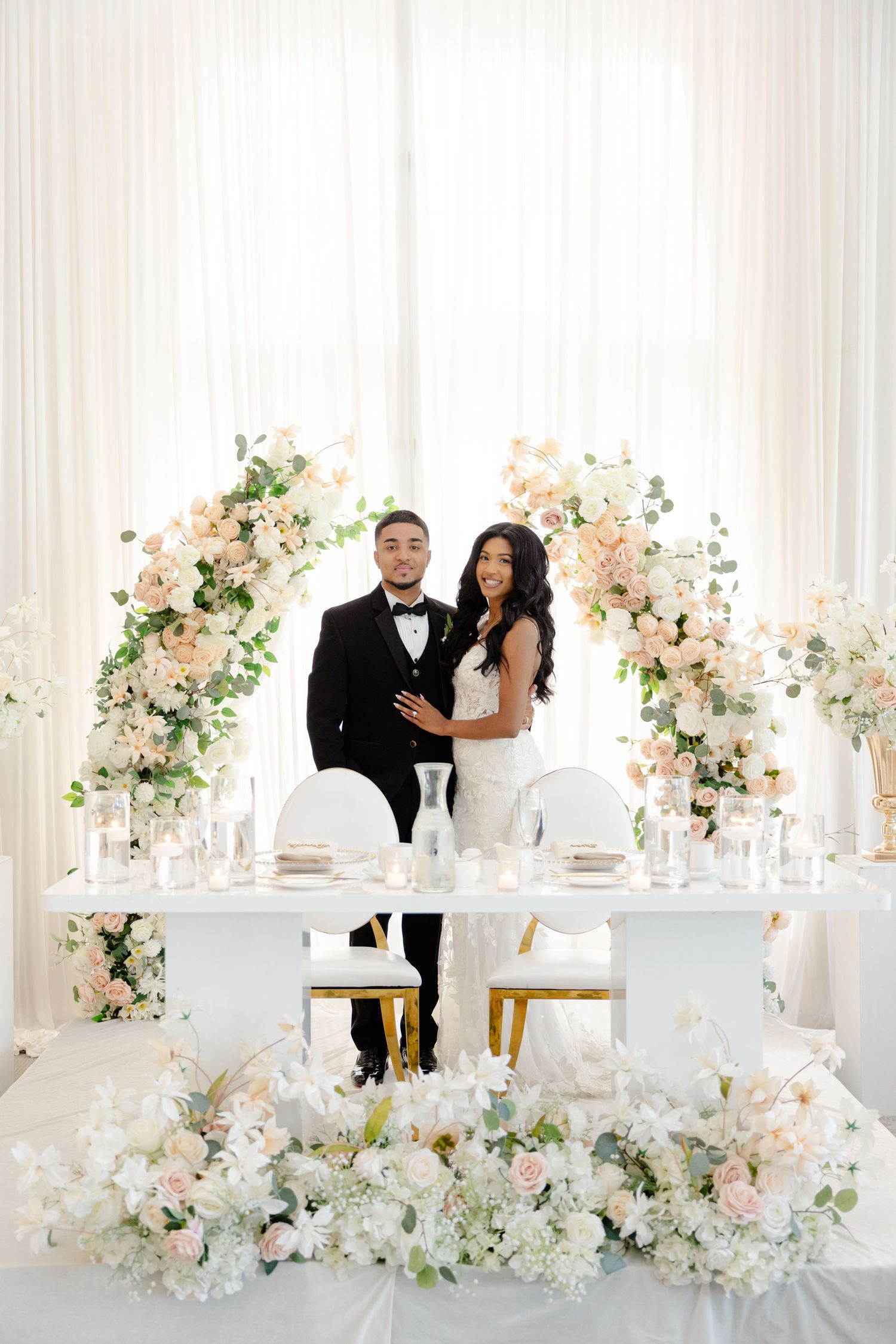 Luxurious sweetheart table decorated with pink and white floral arrangements and elegant place settings.