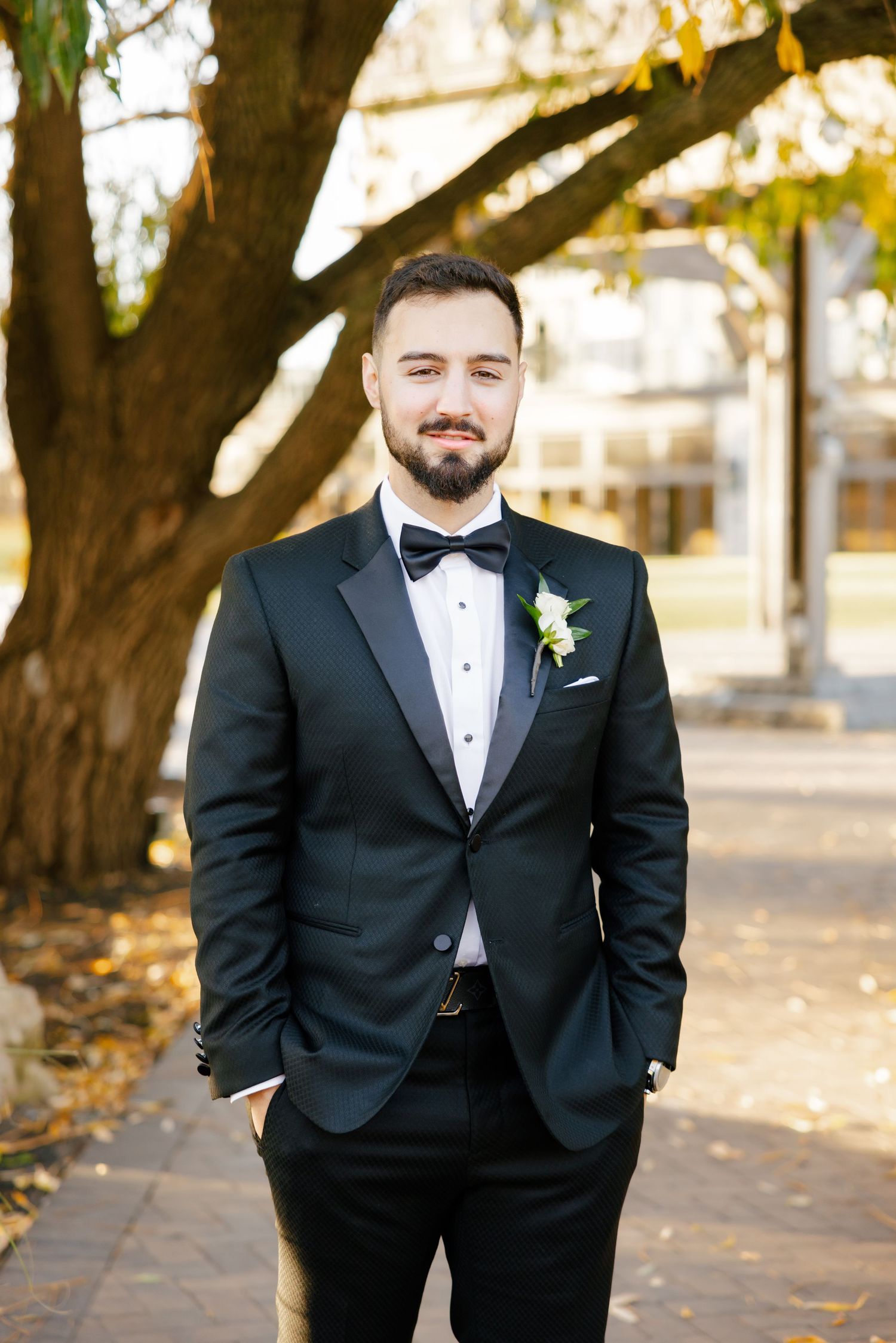 Classic groom portrait in black tuxedo with boutonniere under autumn tree.