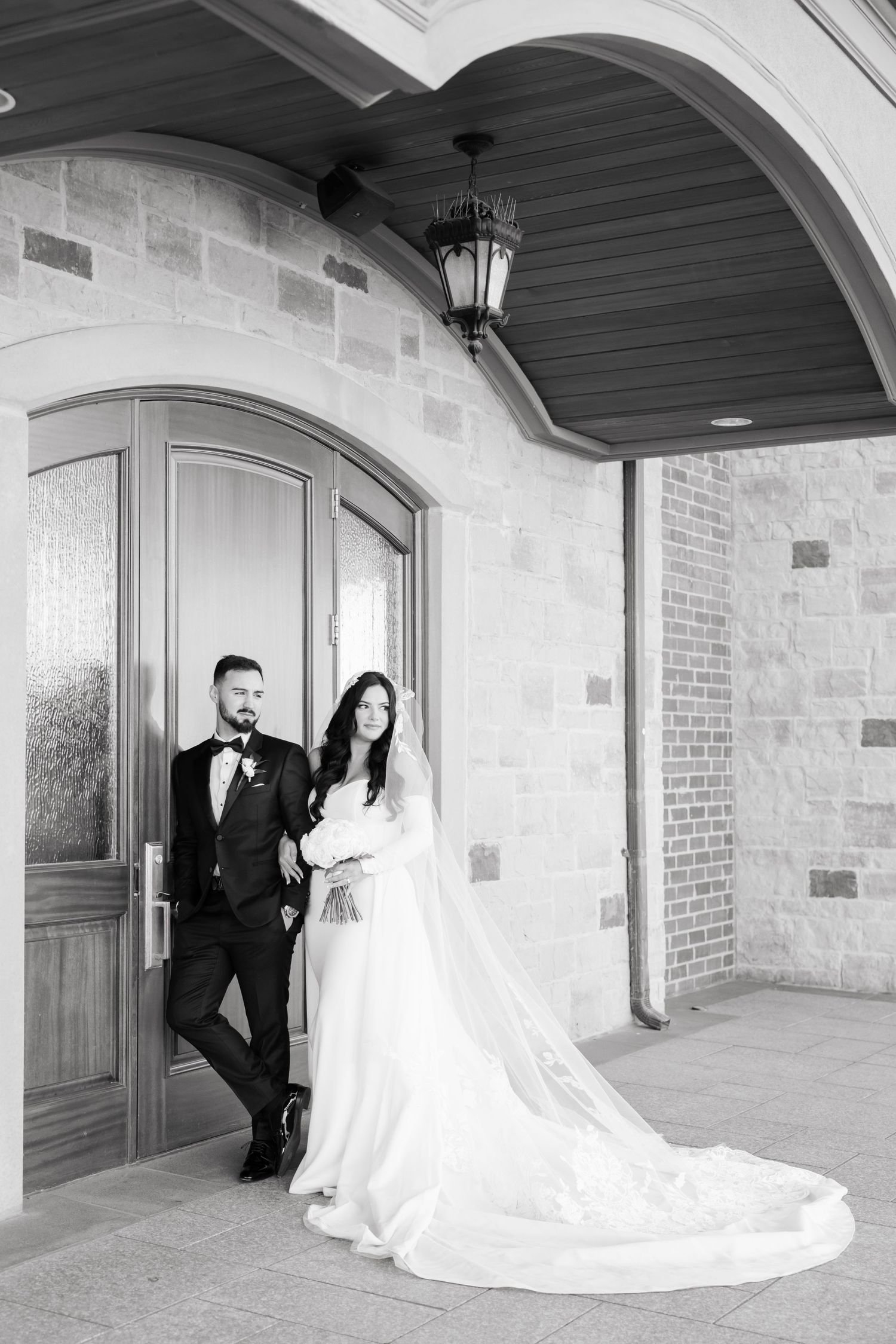Black and white wedding photo of couple posing by elegant wooden door.