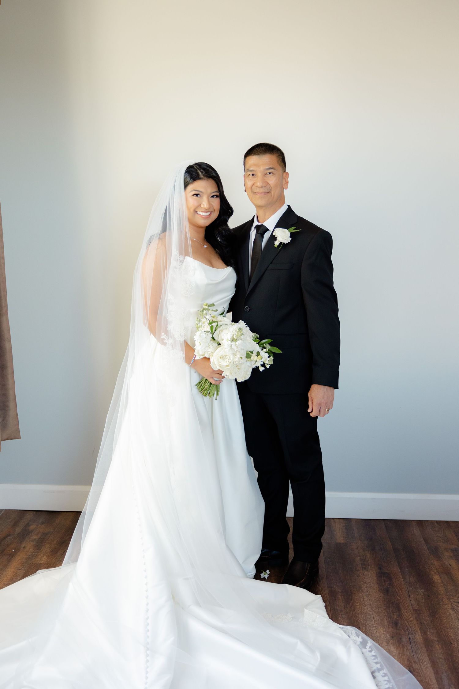 Full length portrait of newlywed couple in traditional wedding attire standing on wooden floor.