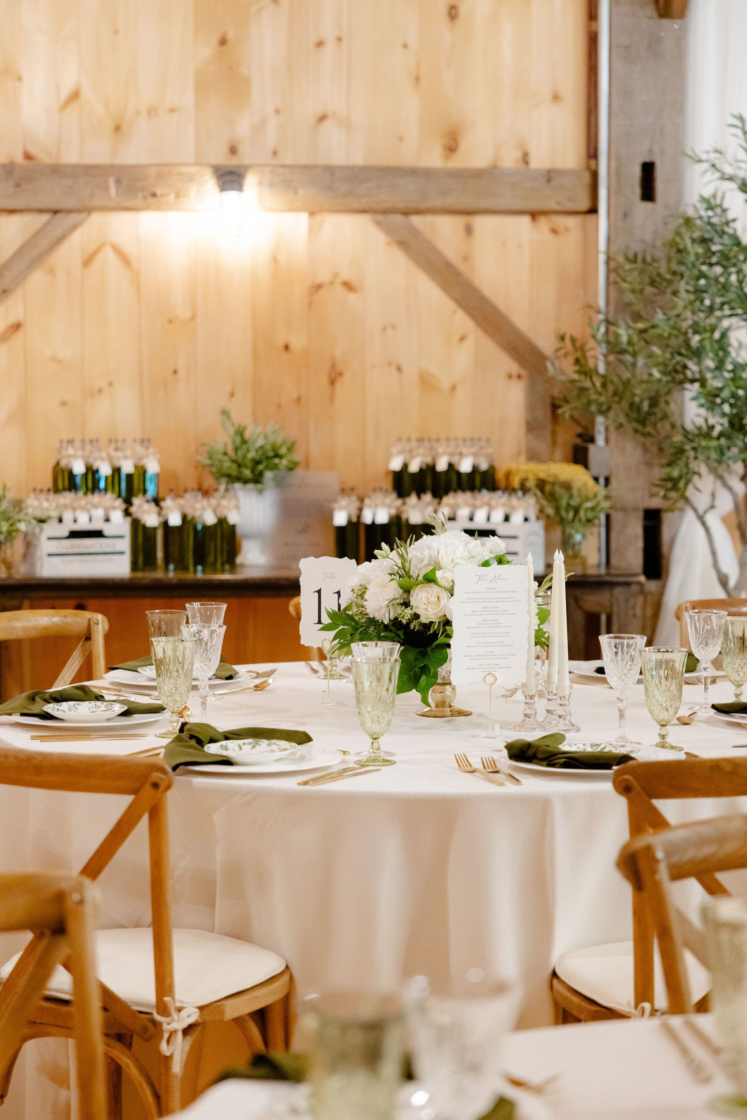 An elegant rustic wedding reception table setting in a barn with white linens and wooden chairs.