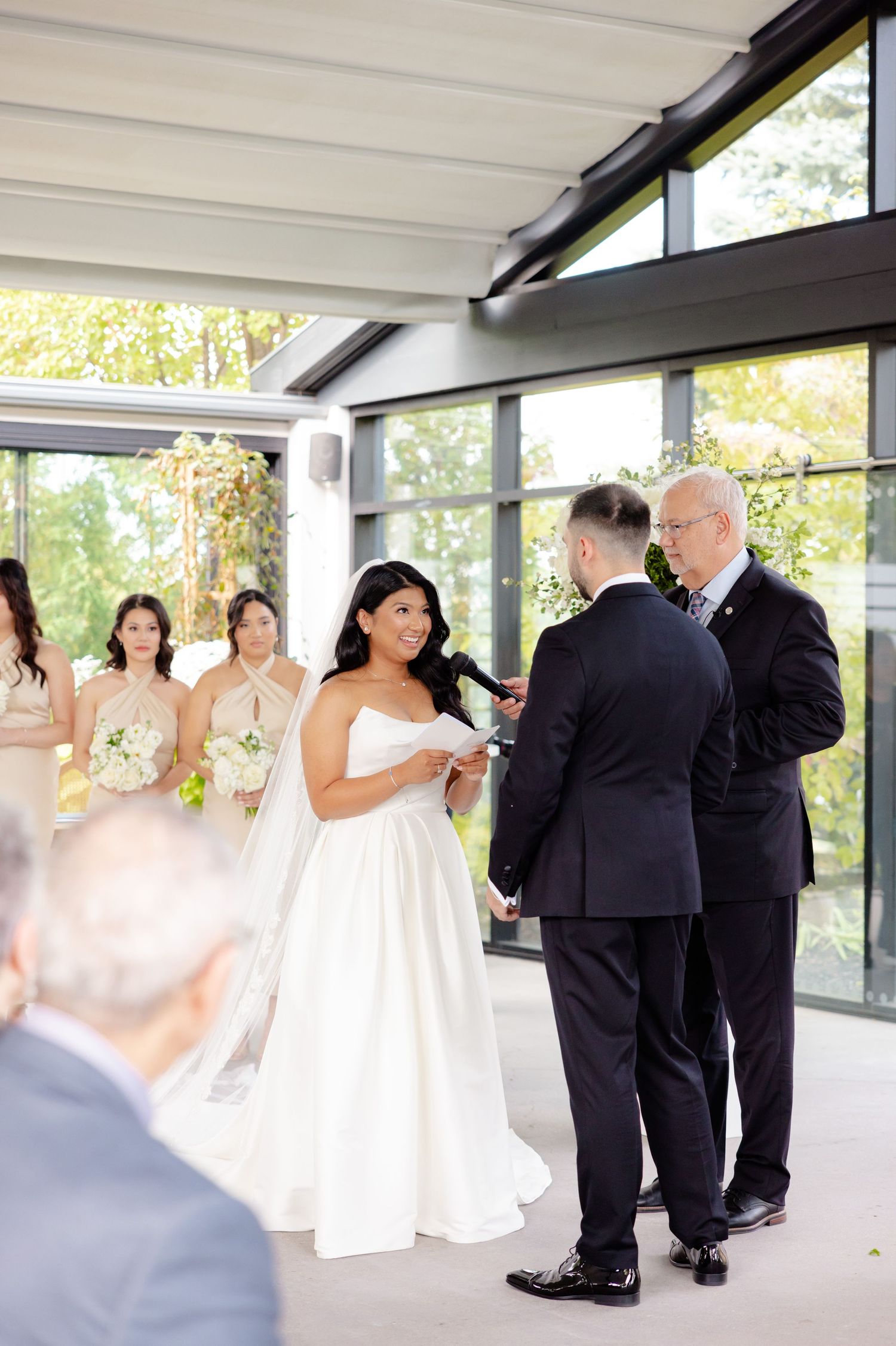 Wedding ceremony in modern venue with floor-to-ceiling windows and natural light.