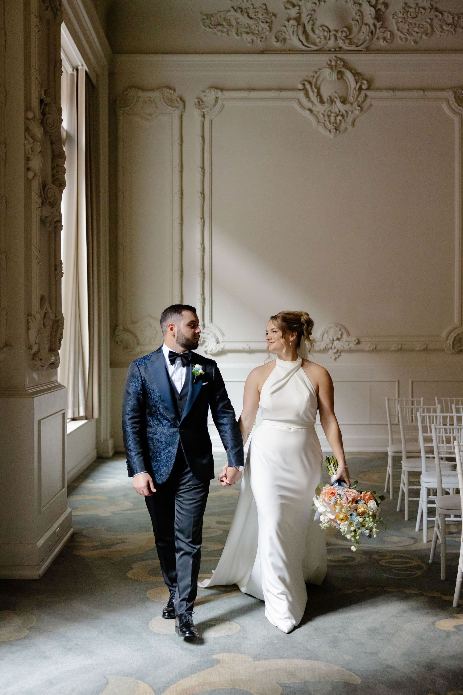 Playful wedding couple dances and laughs together in elegant room with ornate white wall details.