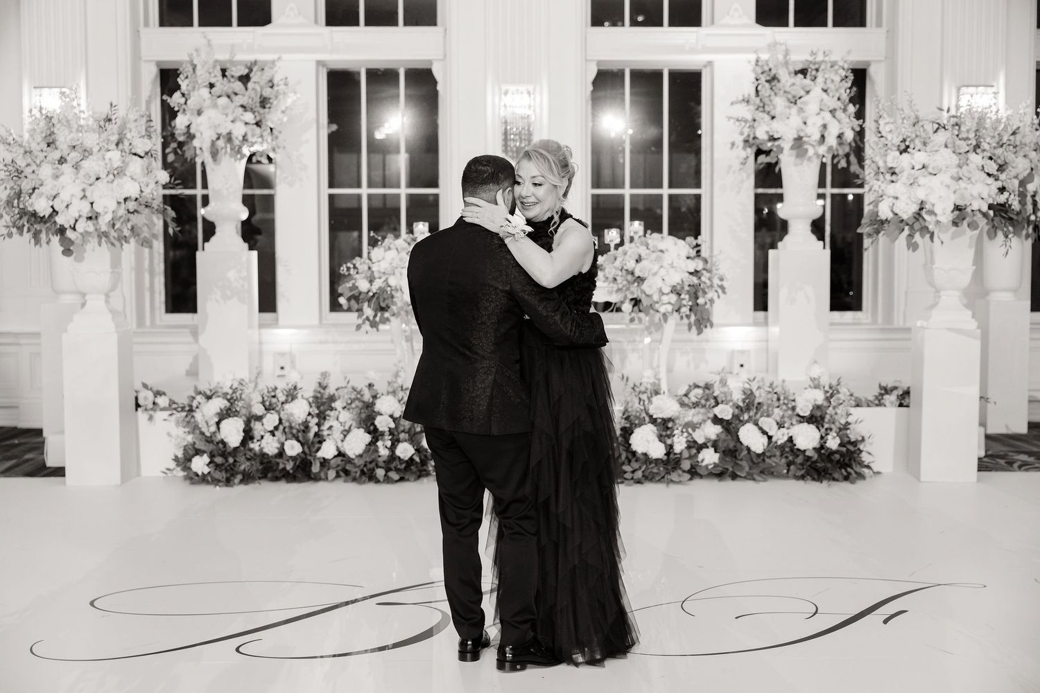 A black and white photo captures an intimate dance moment against a backdrop of elegant floral arrangements.