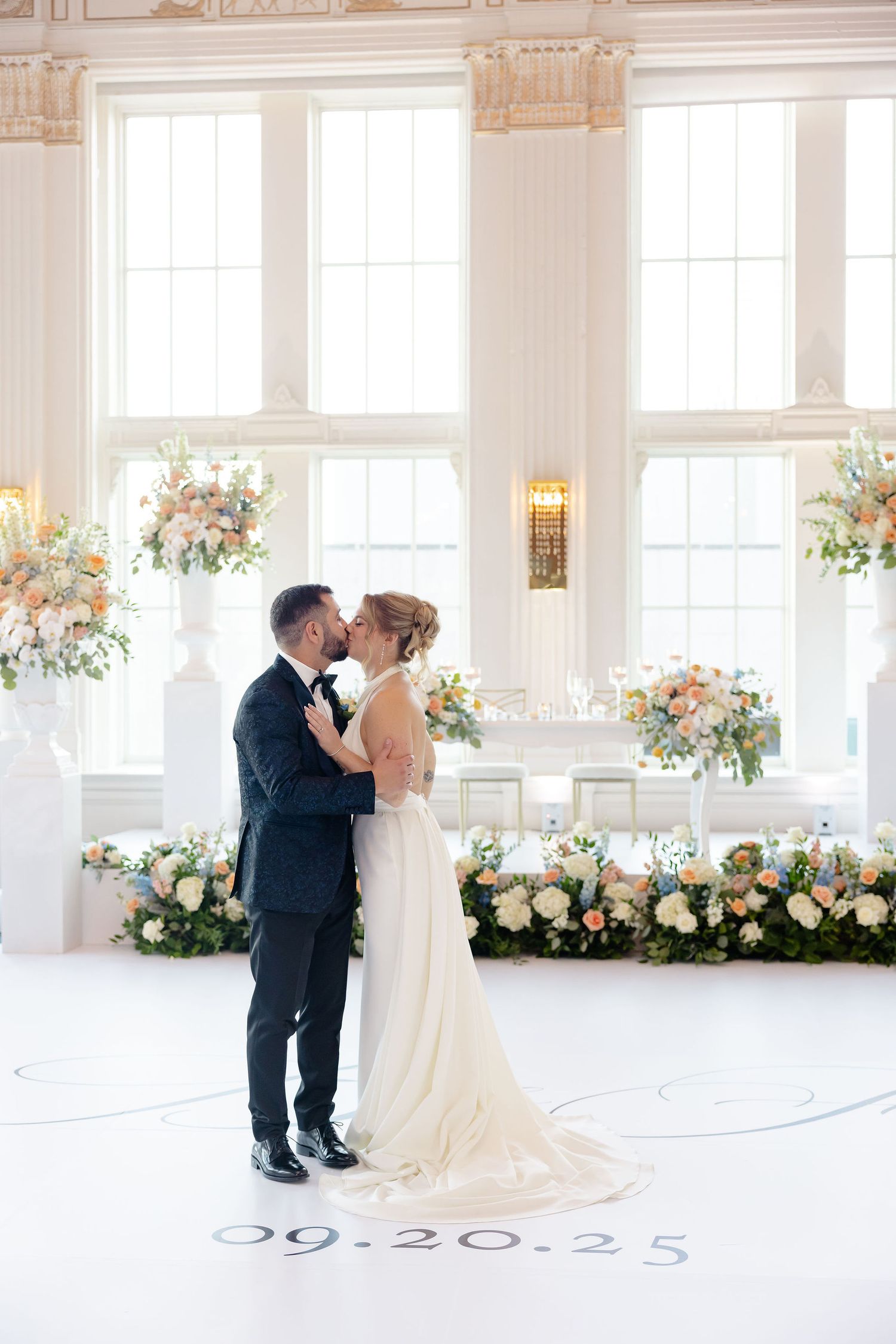 Couple sharing a romantic dance moment in a bright, window-filled reception venue with floral arrangements.