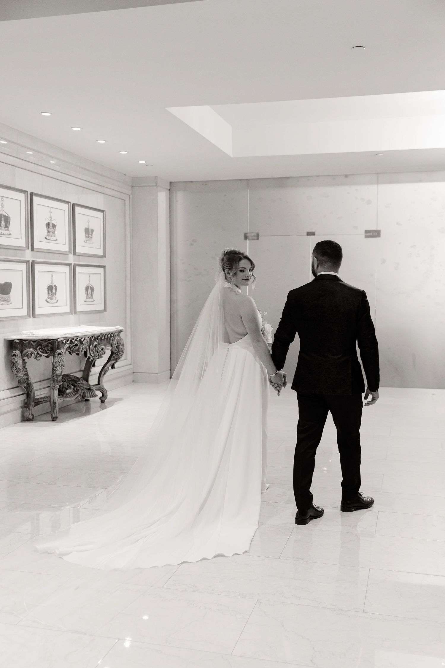 Wedding couple walking through a bright white modern hallway with a flowing bridal train.