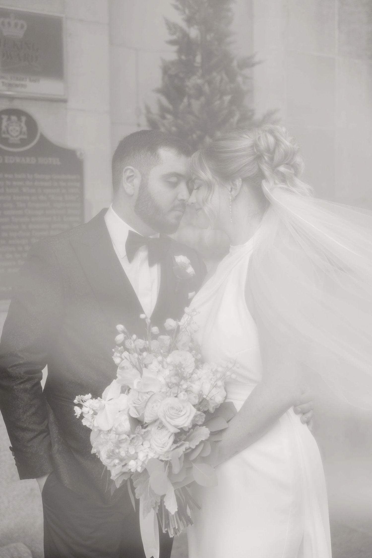 A romantic black and white wedding photo shows a couple embracing with a beautiful floral bouquet.