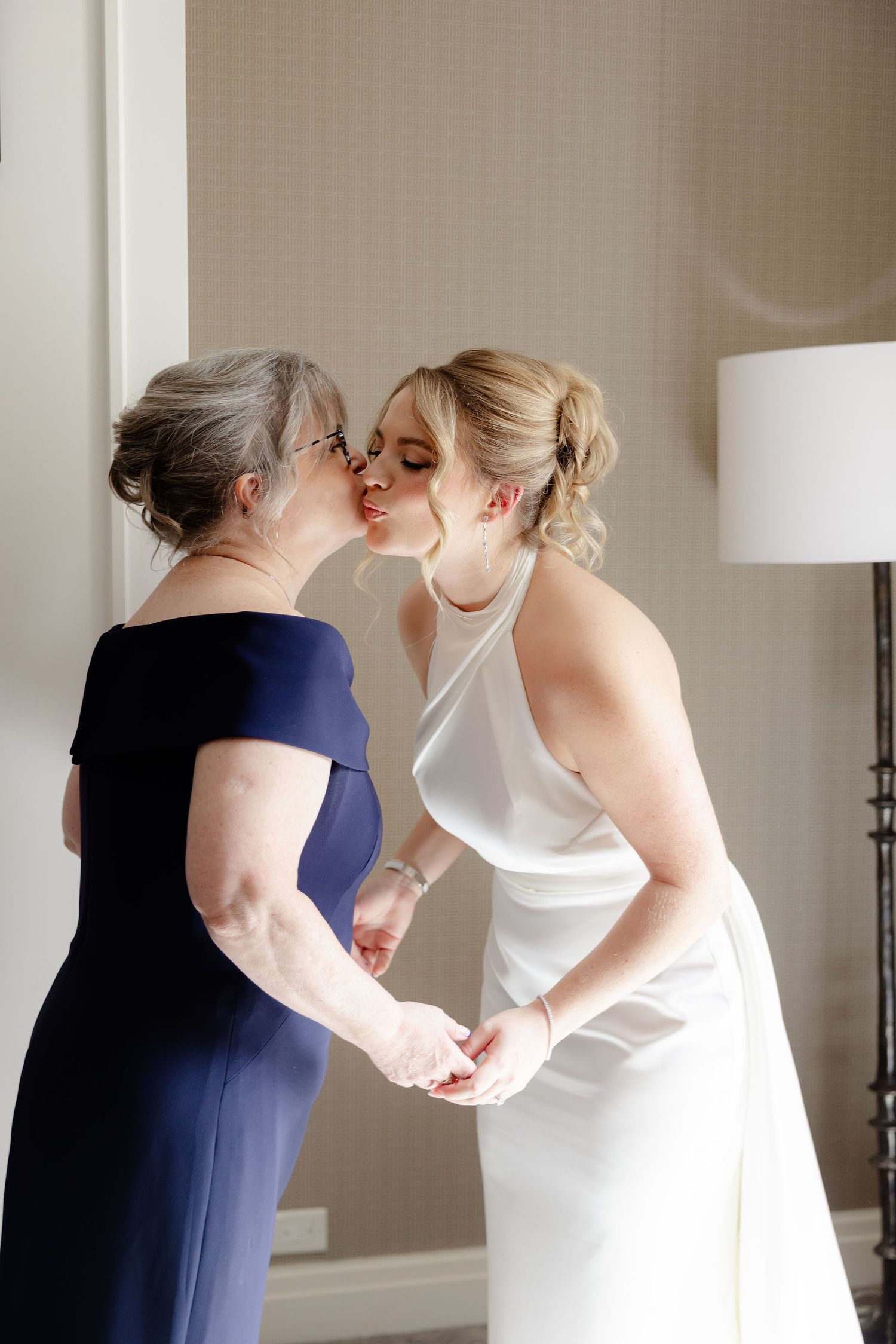 Intimate moment of wedding dress adjustments with attendant in navy blue dress.