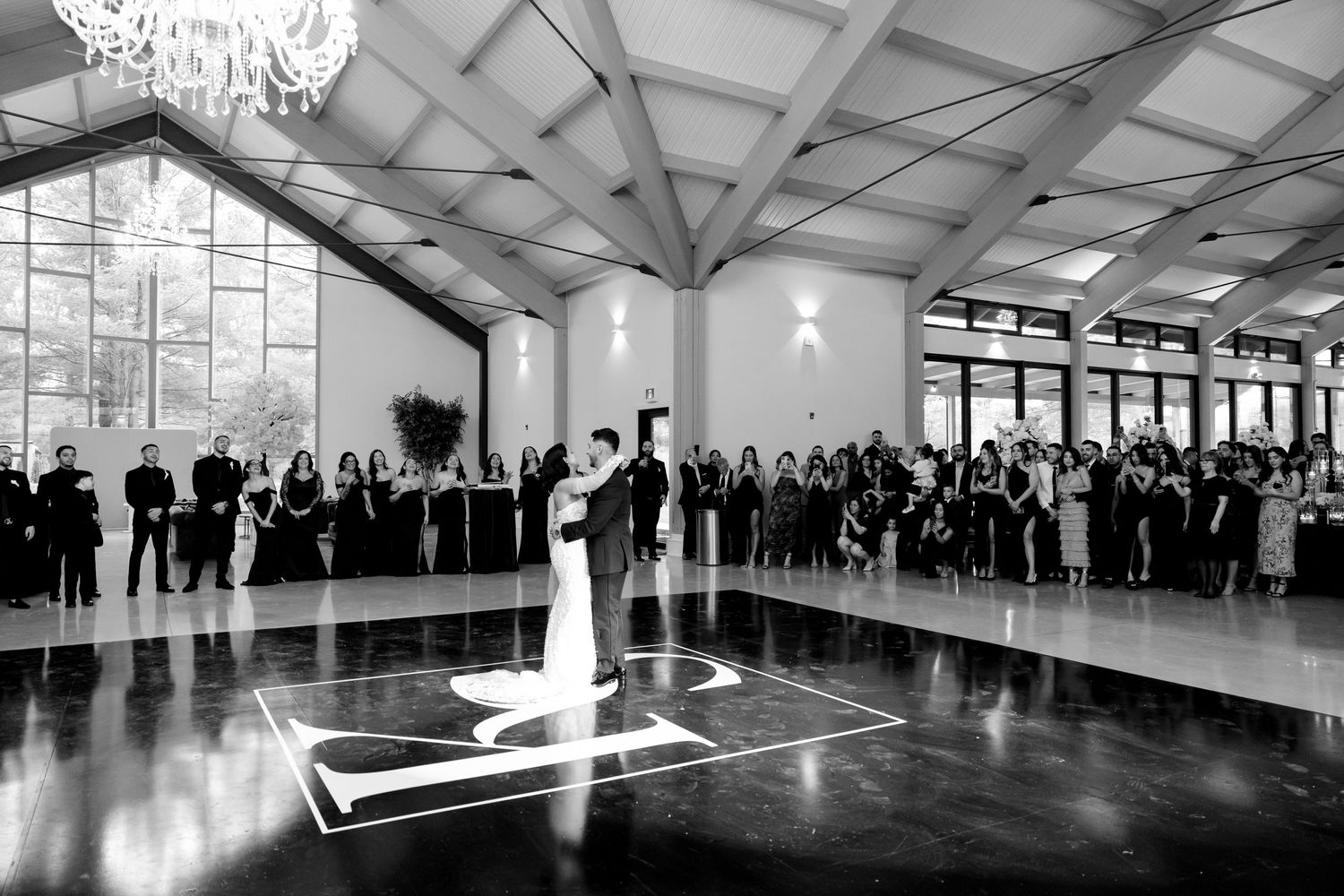 Black and white photo of wedding celebration with guests surrounding illuminated dance floor.