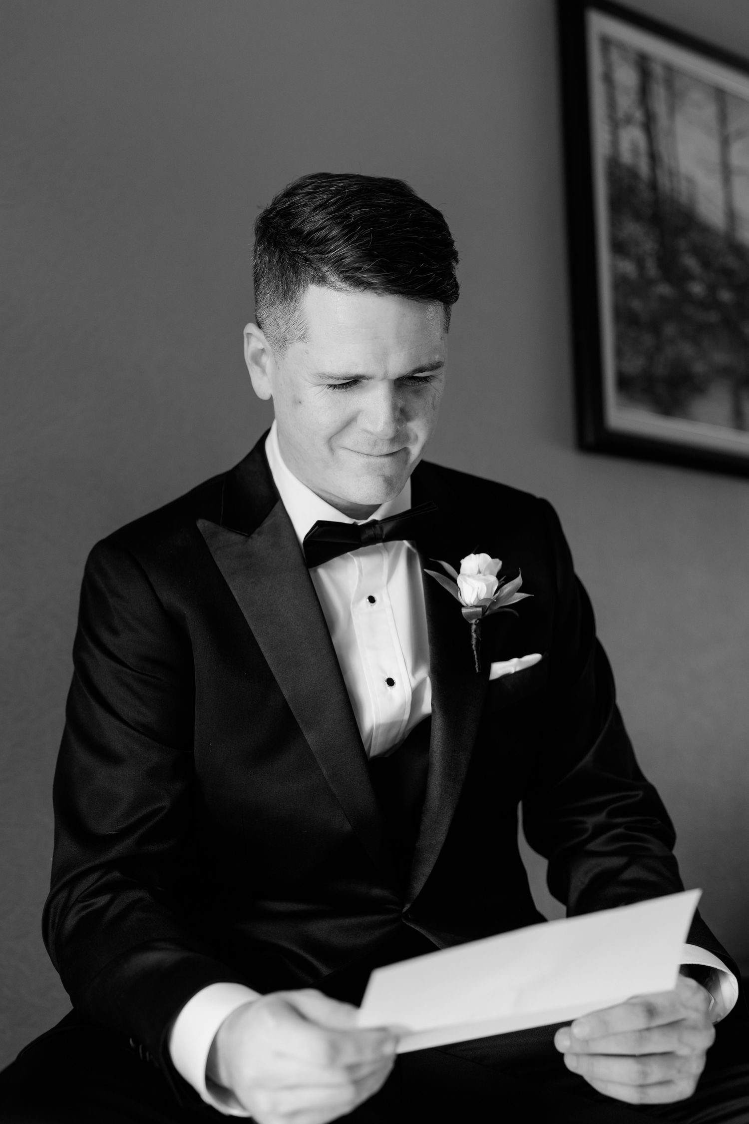 Black and white photo of someone reading a letter while wearing a formal tuxedo.