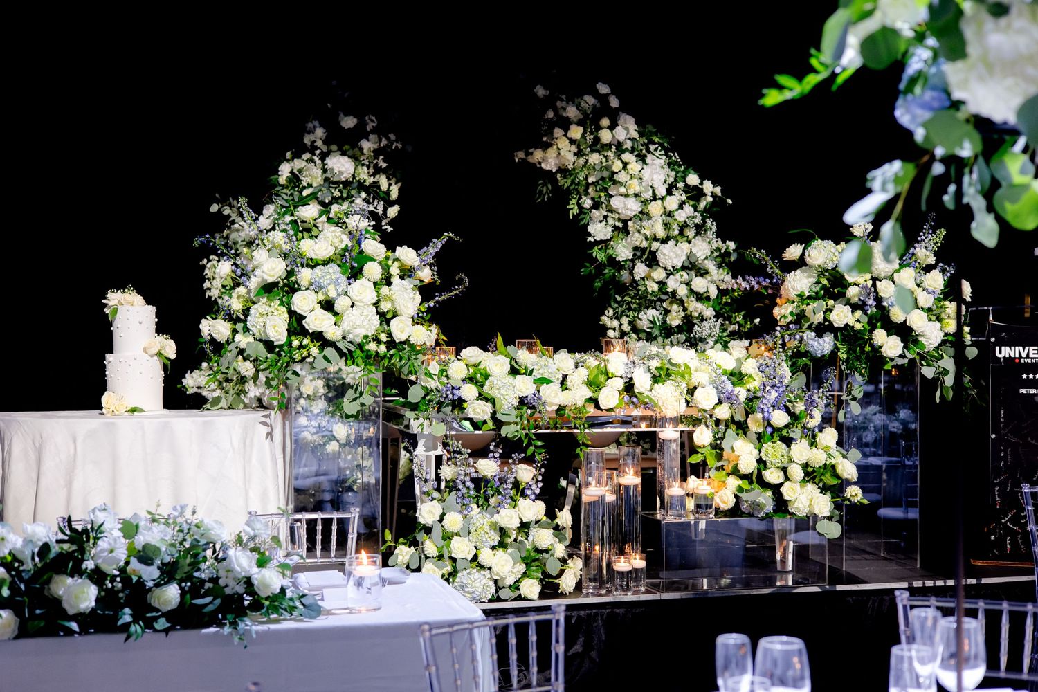 Luxurious white floral wedding arch display with candles and elegant table settings.