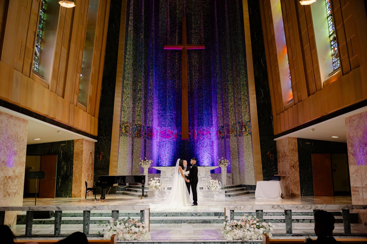 Church wedding ceremony with dramatic purple lighting and cross backdrop on elevated altar.