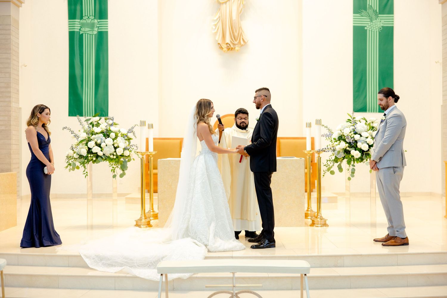 Wedding ceremony in progress at a modern church altar with green accents and white flowers.