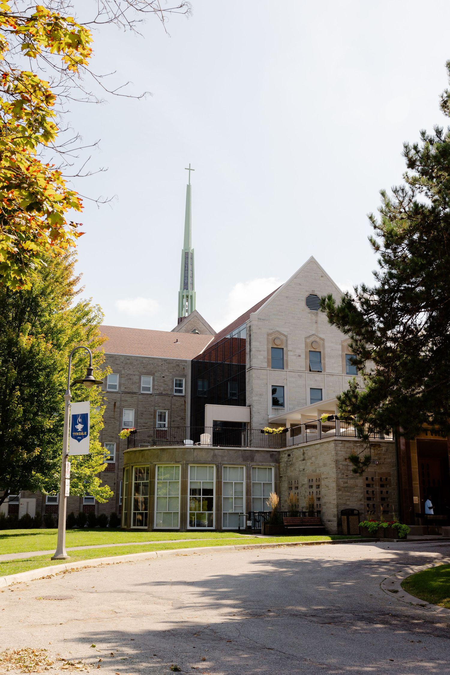 Contemporary church exterior with stone walls and tall green spire against cloudy sky.