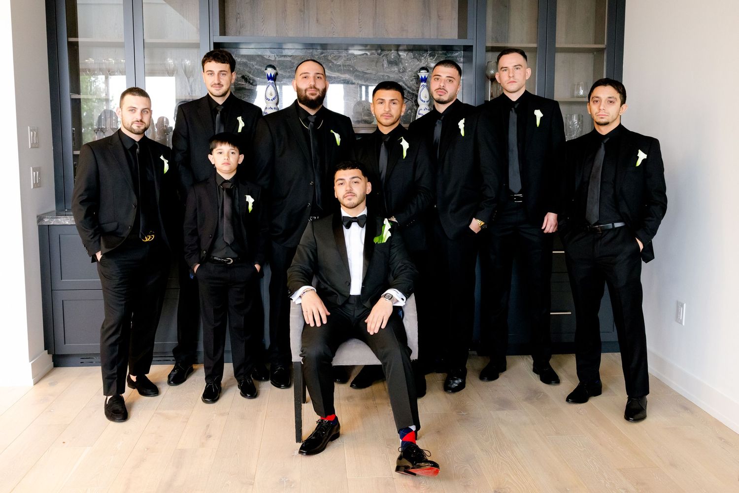 Groomsmen in black suits and tuxedos pose together in modern interior setting.