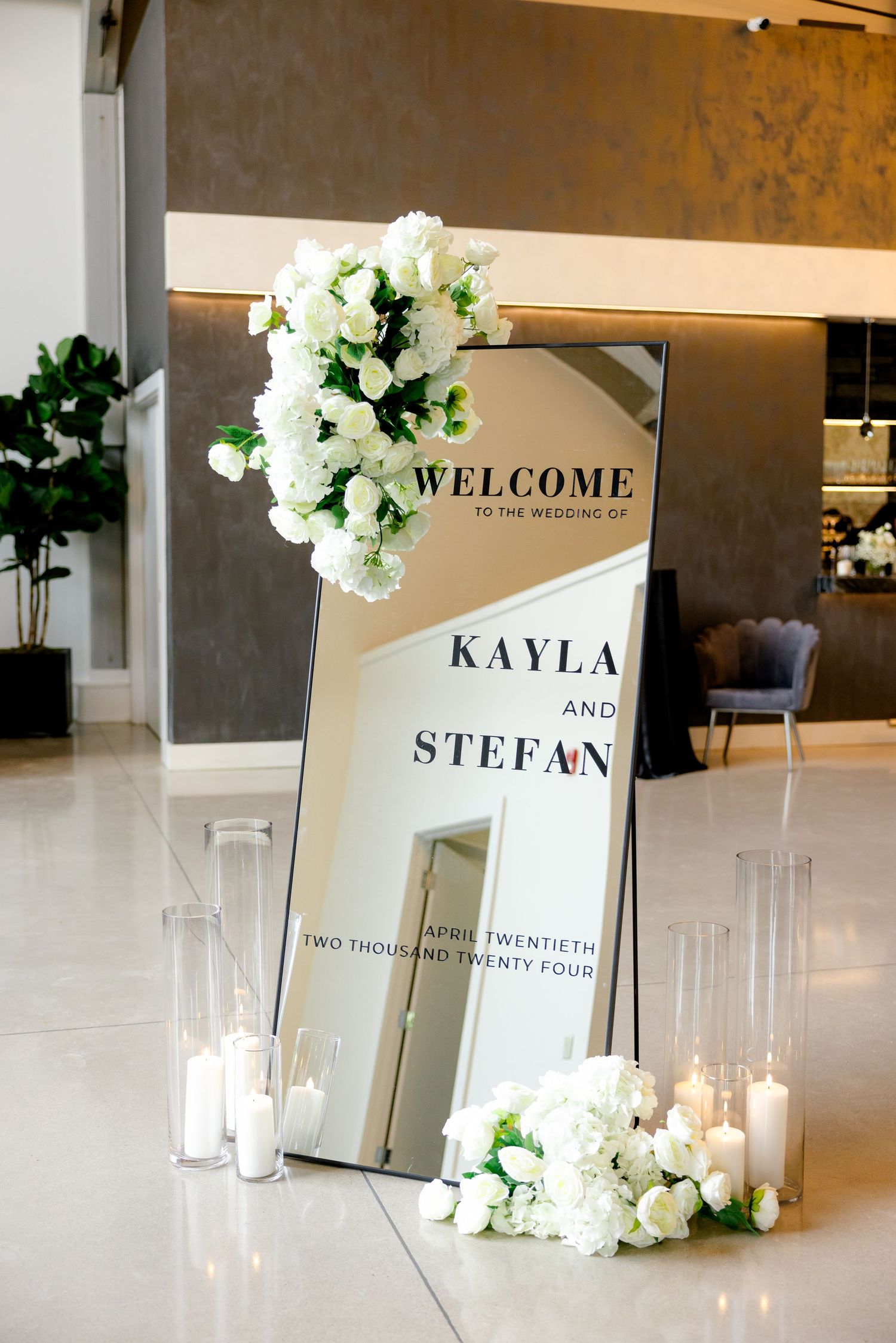 Modern mirrored wedding welcome sign decorated with white flowers and candles.