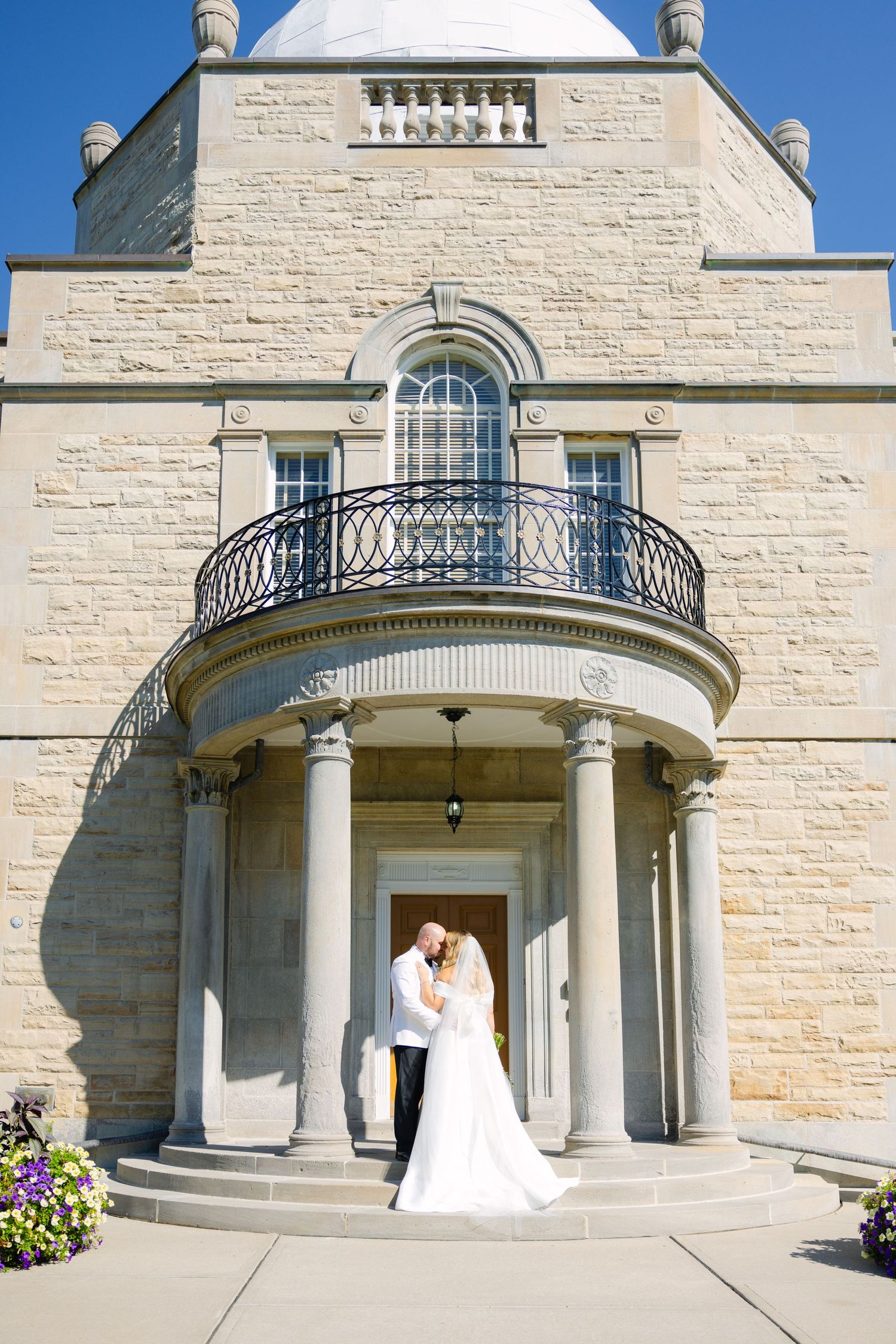 White stone building with curved balcony and classical columns creates a romantic wedding backdrop.