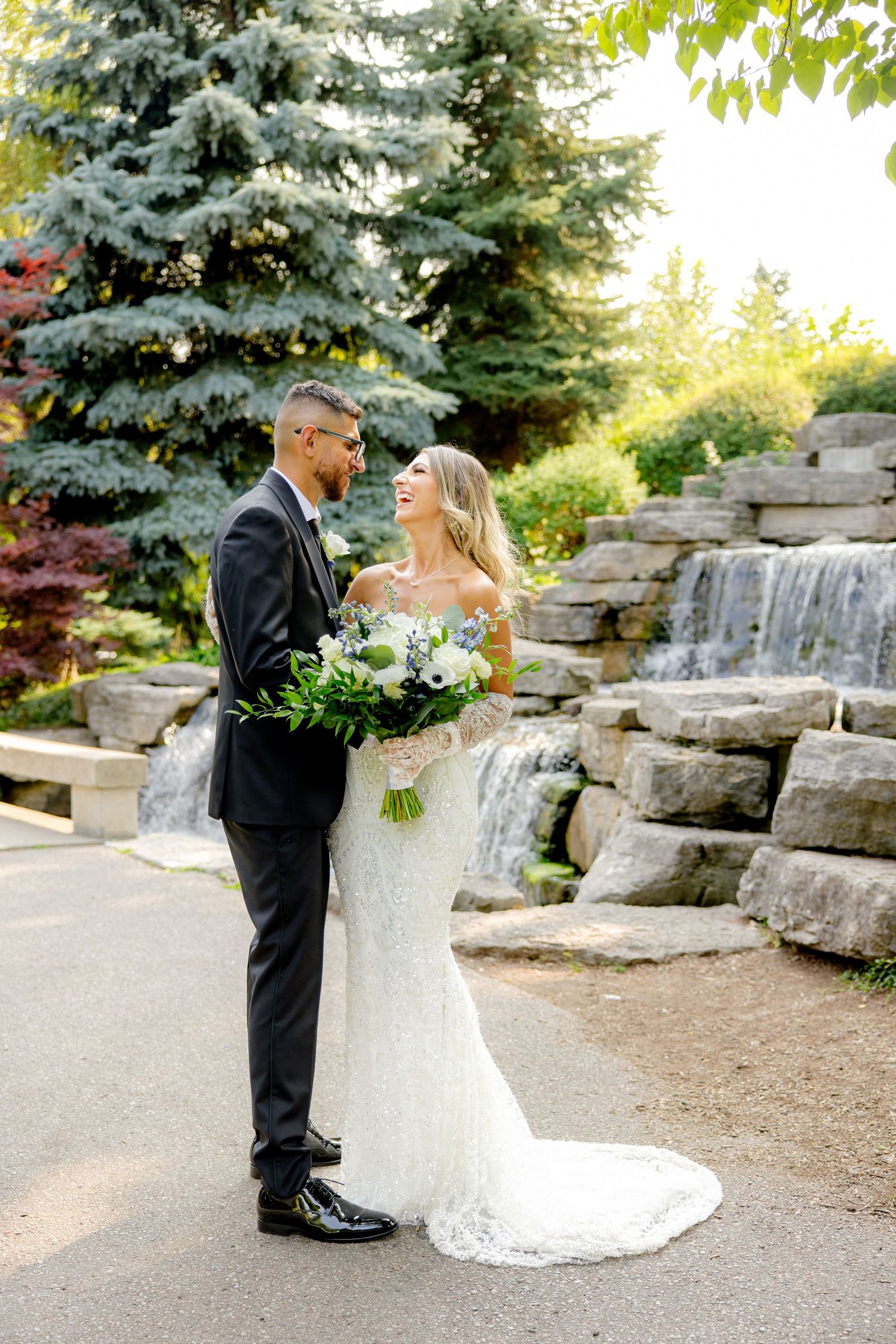 A wedding portrait in front of a cascading stone waterfall with blue spruce trees in the background.