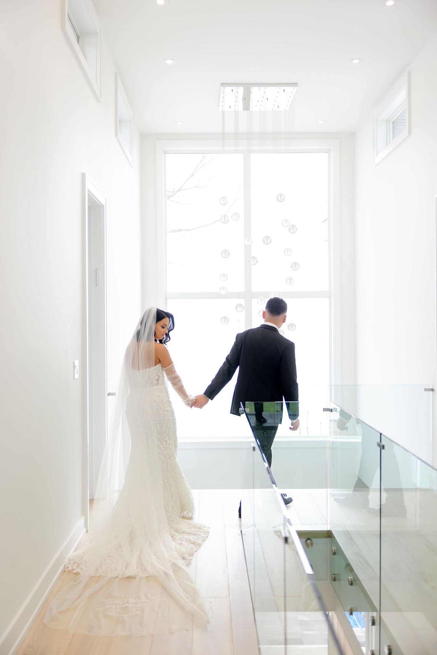 Couple walks hand in hand down modern white hallway with glass railings.